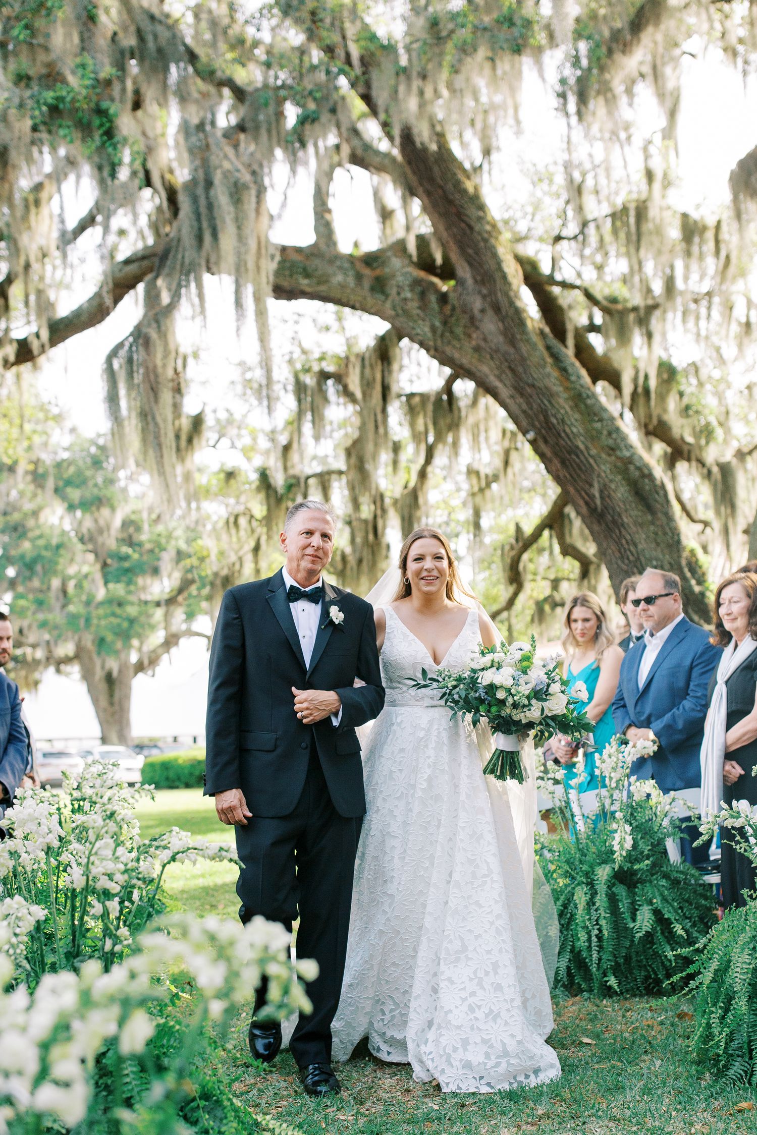 Outdoor wedding ceremony under Spanish moss with white flowers lining the aisle.