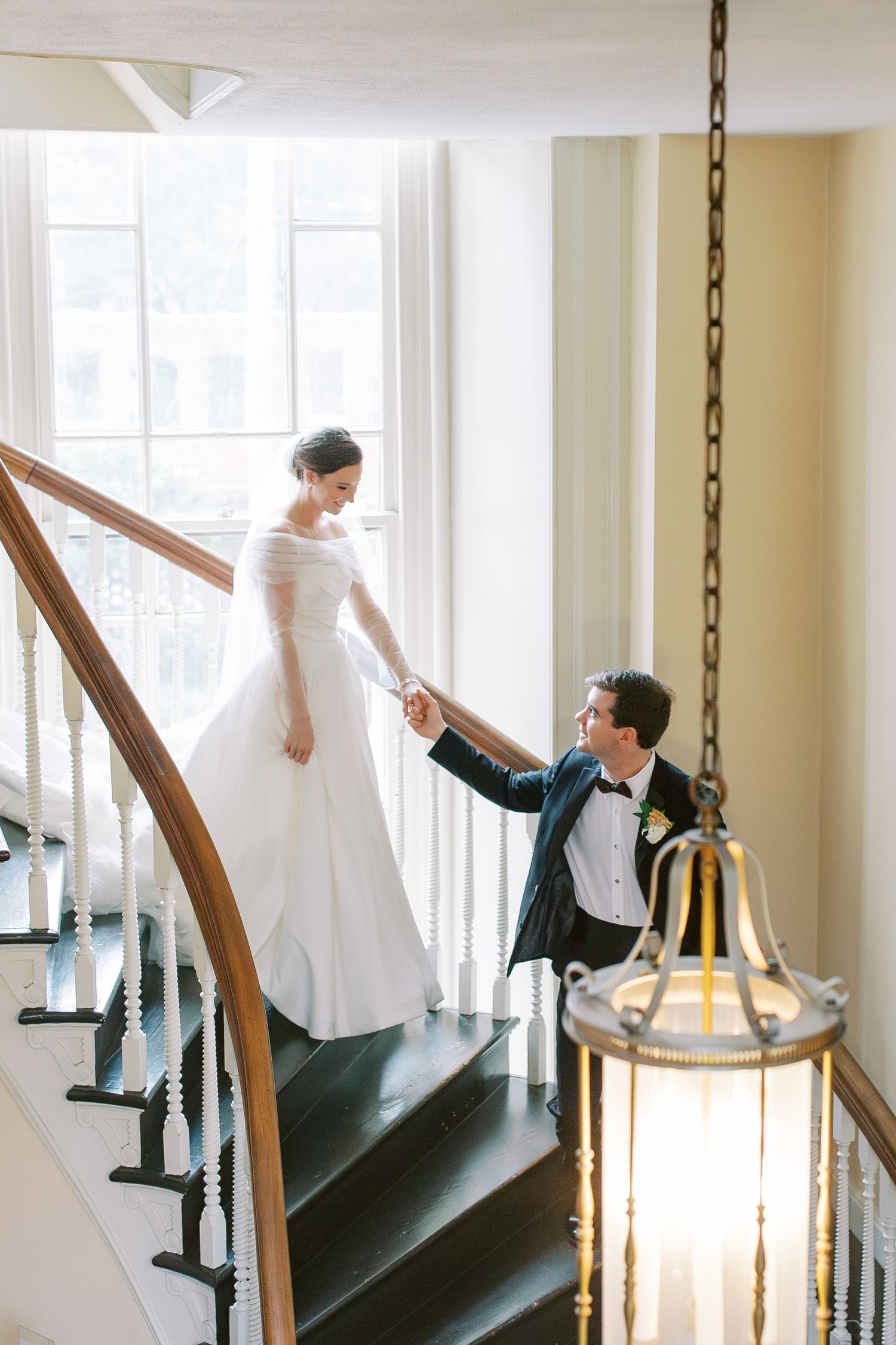 A romantic moment on an elegant staircase with sweeping wooden railings and a decorative hanging lantern.