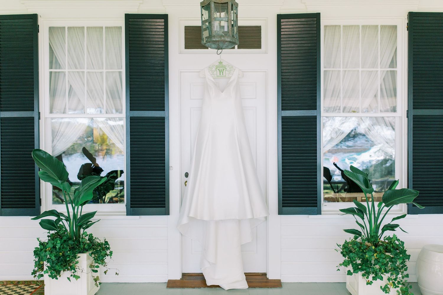 White wedding dress hanging between green shutters on classic Southern home exterior.