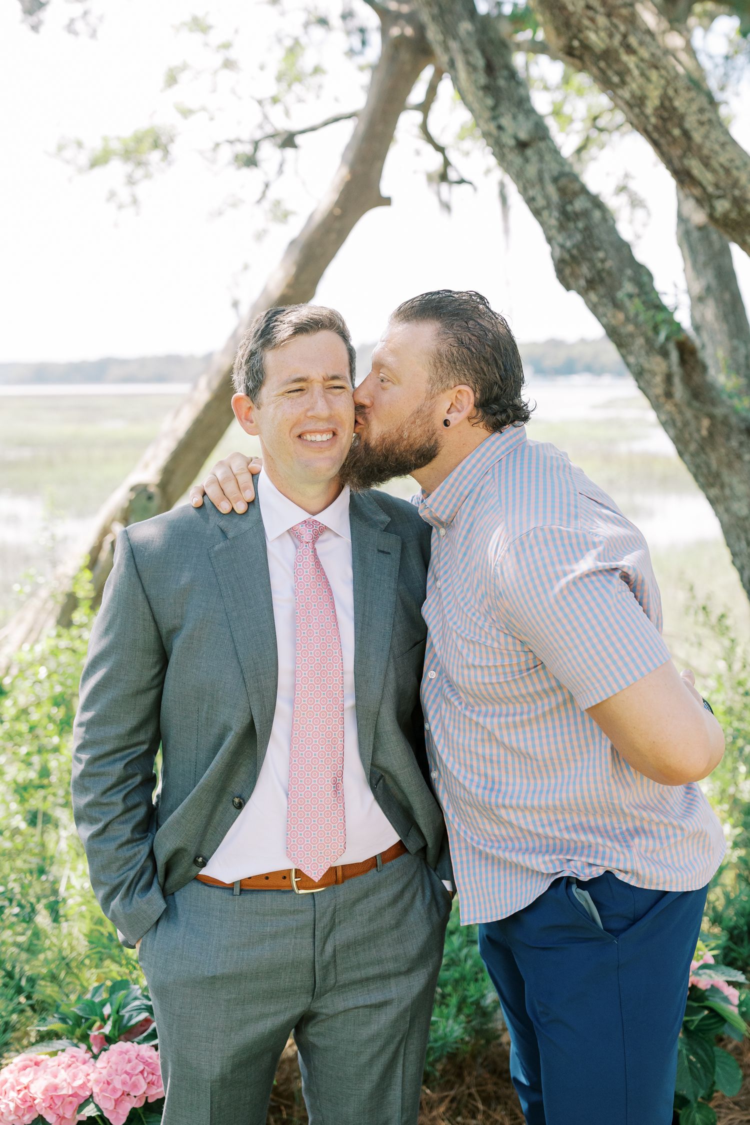 Two people sharing intimate moments outdoors under trees with pink ties and casual attire.
