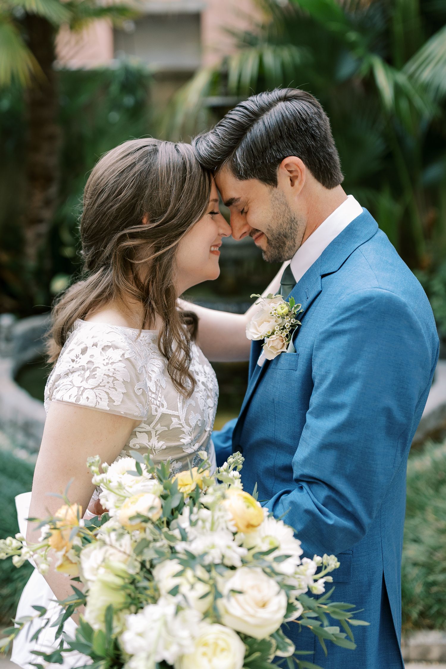 Romantic wedding couple shares intimate moments in a lush garden setting with soft yellow and white floral bouquet.