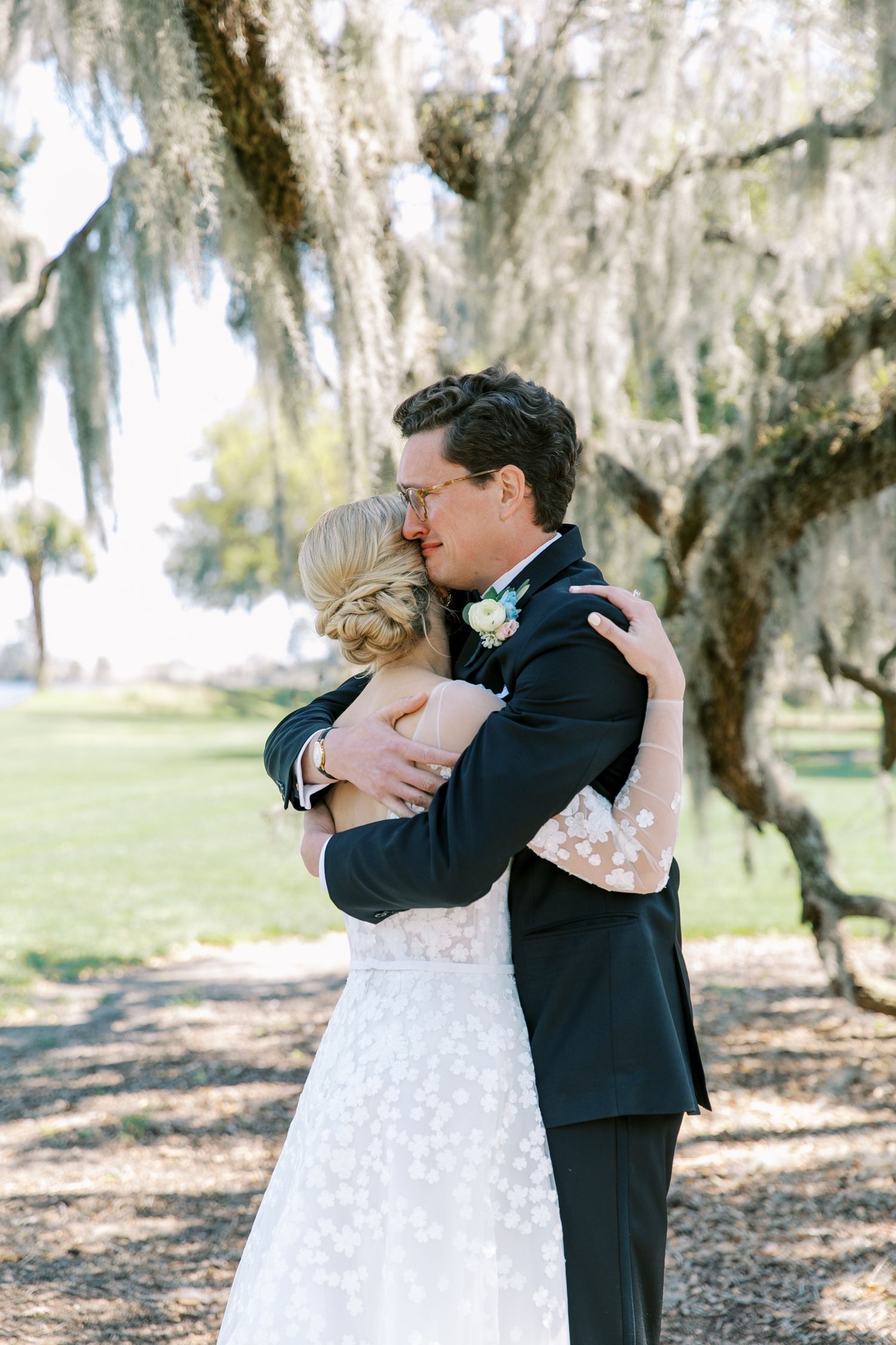 A romantic couple shares a tender kiss under Spanish moss draped trees in a dreamy outdoor setting.