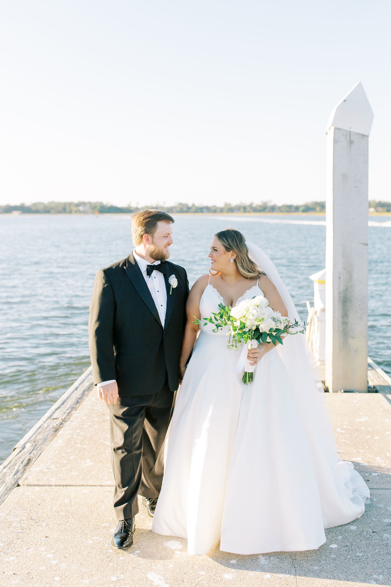 Wedding couple standing on waterfront dock with boats in the background.