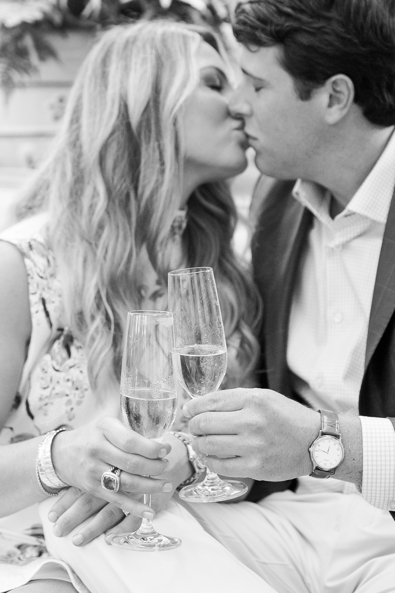 Black and white romantic celebration photo with champagne glasses being toasted during an intimate moment.