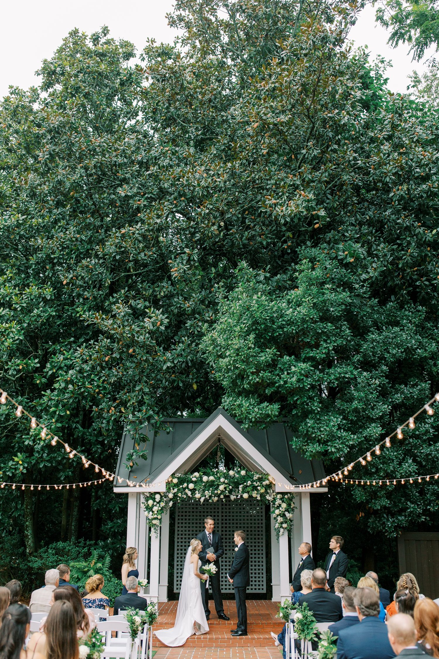 Garden wedding ceremony under wooden arch with string lights and lush greenery in Atlanta.