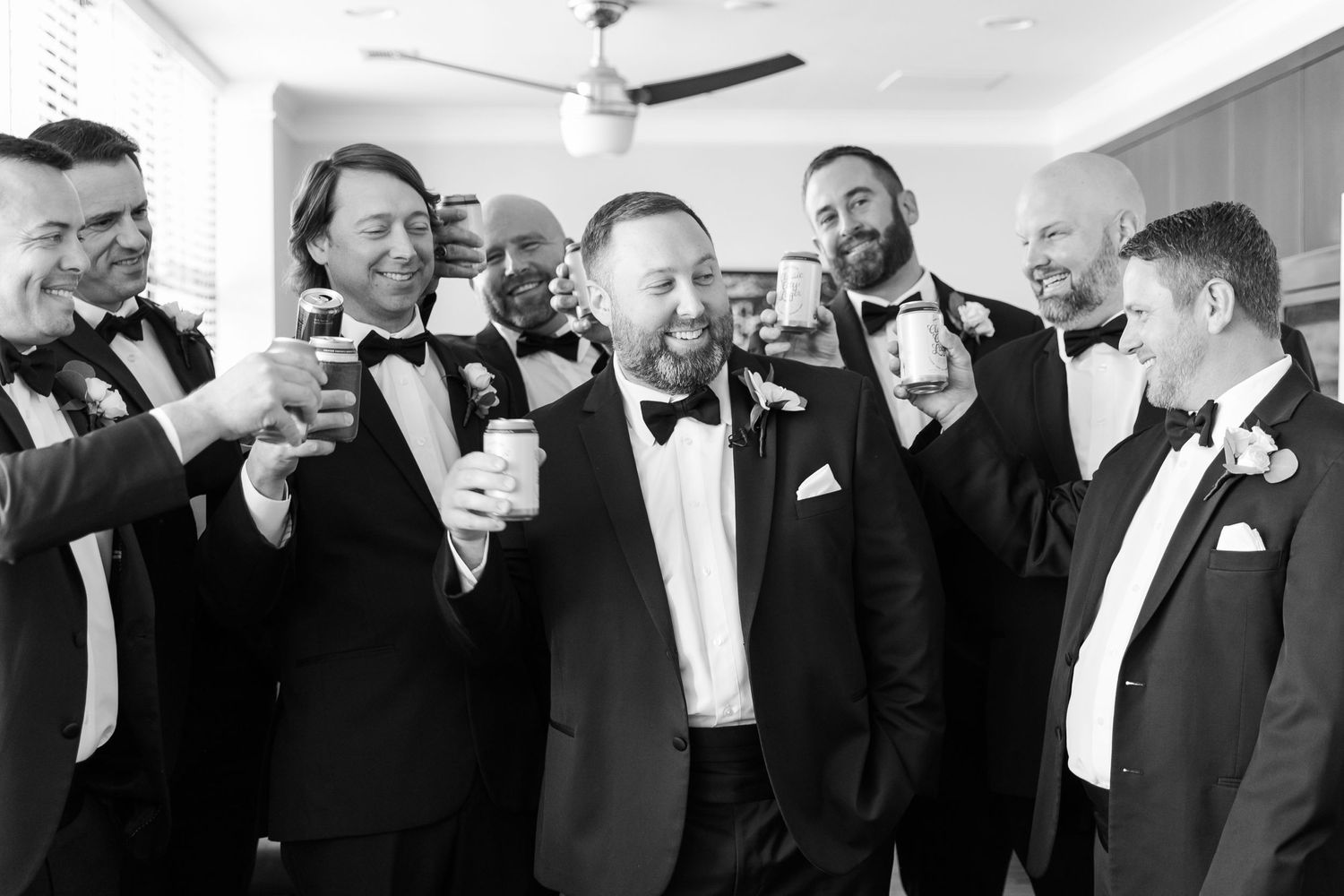 Groomsmen in black tuxedos raising glasses in celebration at wedding reception.