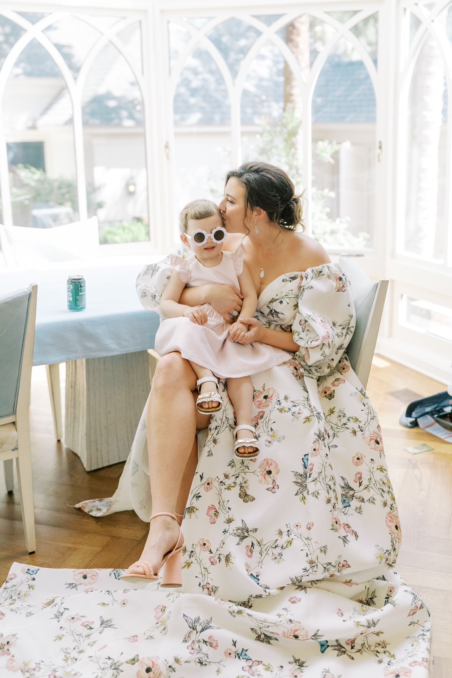 A tender moment between parent and child sitting in sunlit room with floral dress and white decor.