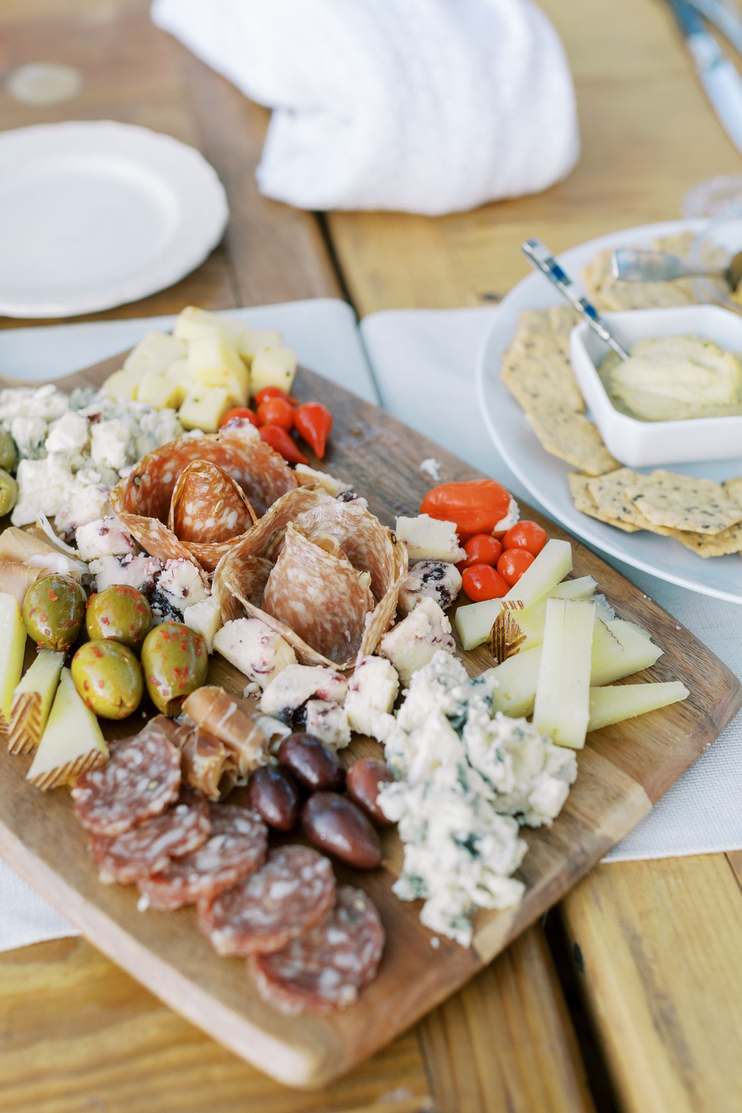 Appetizer charcuterie board with meats, cheeses, pickles and crackers served on wooden platter.