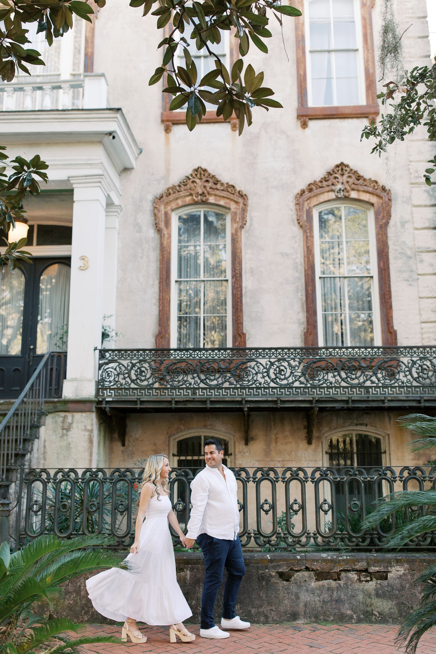 Couple posing in front of historic building with ornate ironwork balcony and magnolia leaves in downtown Savannah