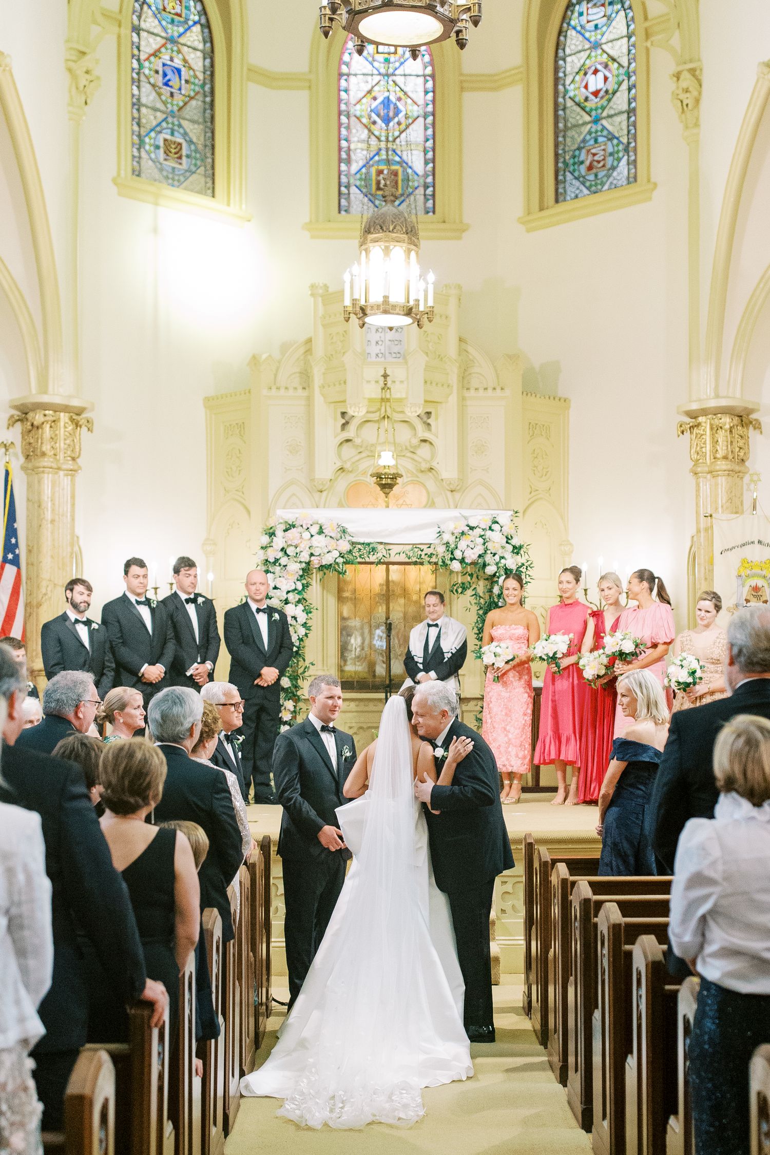 An elegant church wedding ceremony with beautiful stained glass windows and floral arch decorations at the altar at Mickve Israel.
