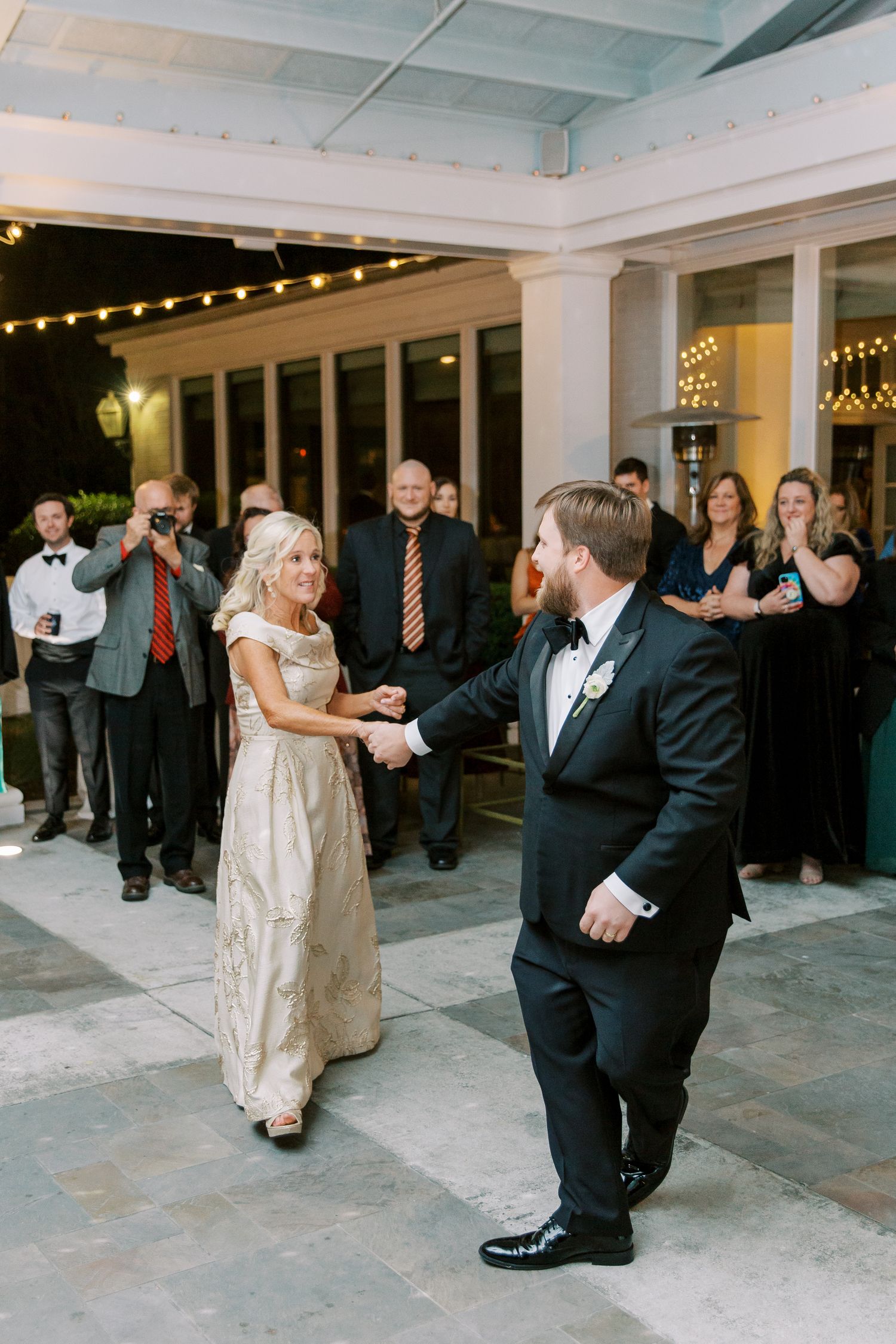 Wedding guests watch a couple dancing on an outdoor patio decorated with string lights.