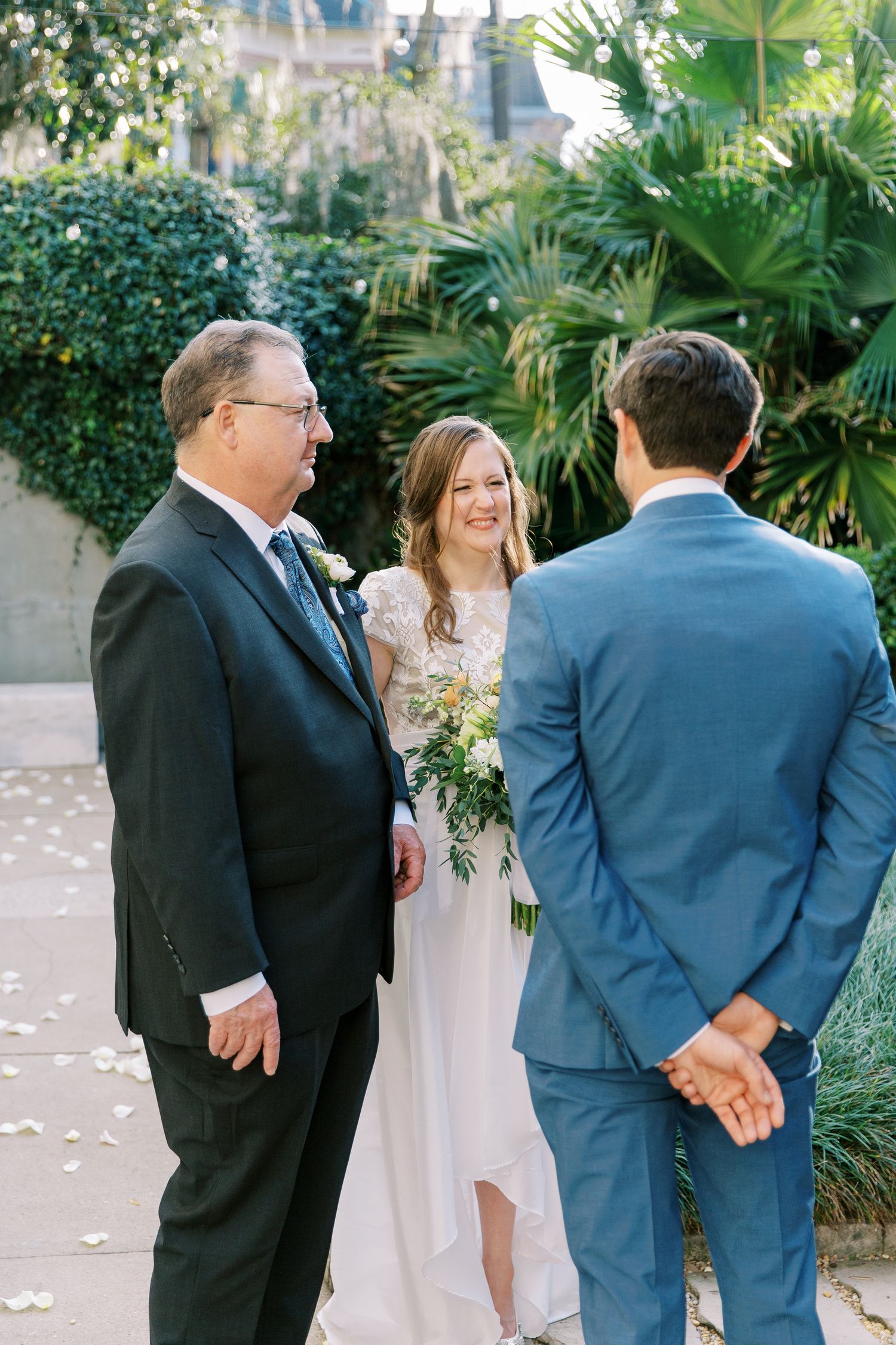 A wedding ceremony scene in a lush garden setting with guests and wedding party gathered around.