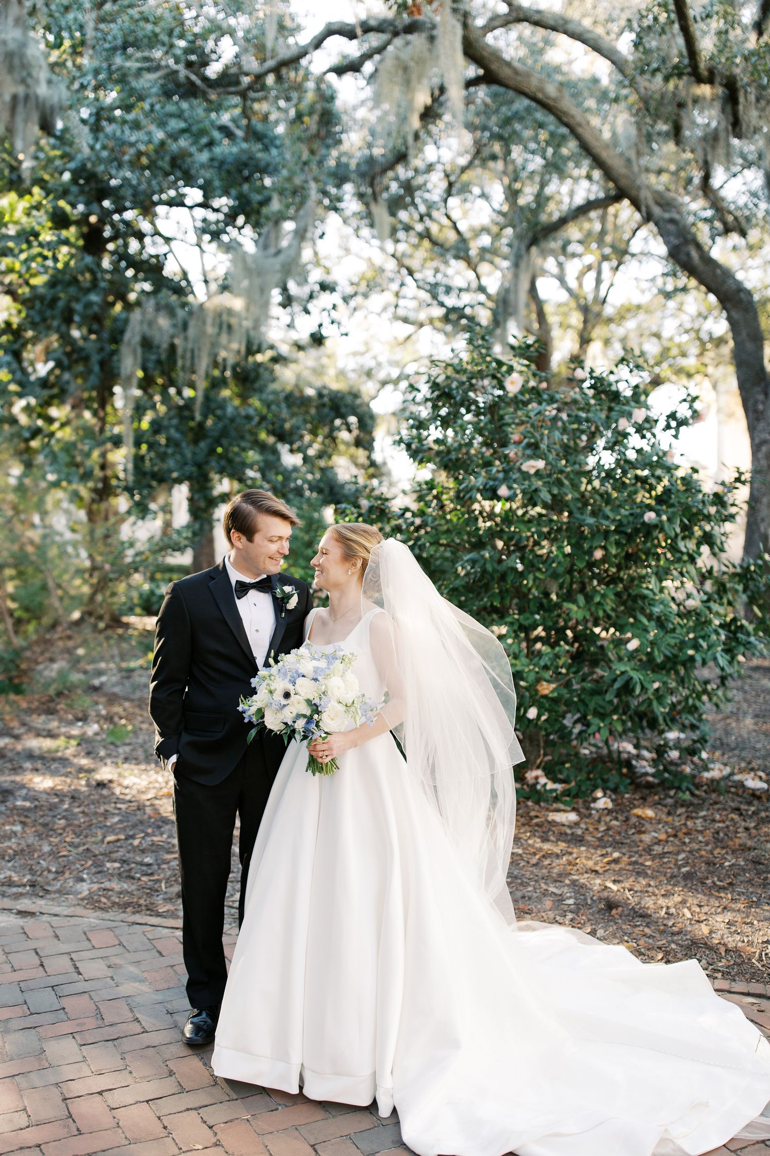 A romantic wedding portrait in a garden setting with oak trees and brick pathways.