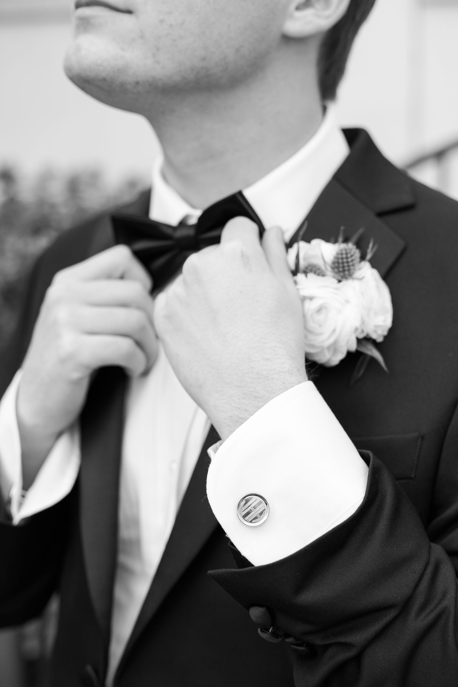 Groomsmen adjusting bow ties and boutonnieres in black and white formal attire.