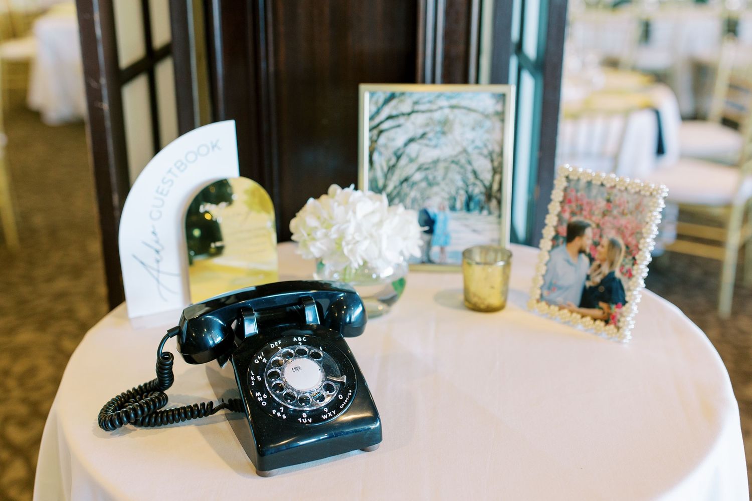 Vintage black rotary phone and framed photos displayed on white table at wedding reception.