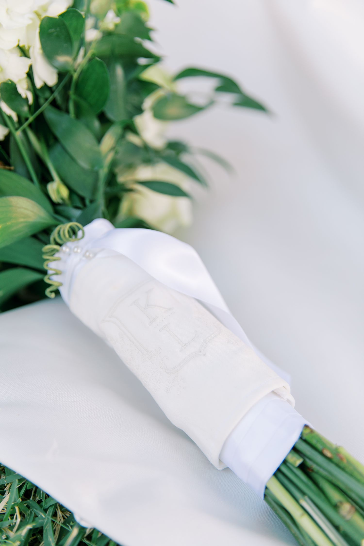 Wedding bouquet wrapped in white ribbon against a light background.