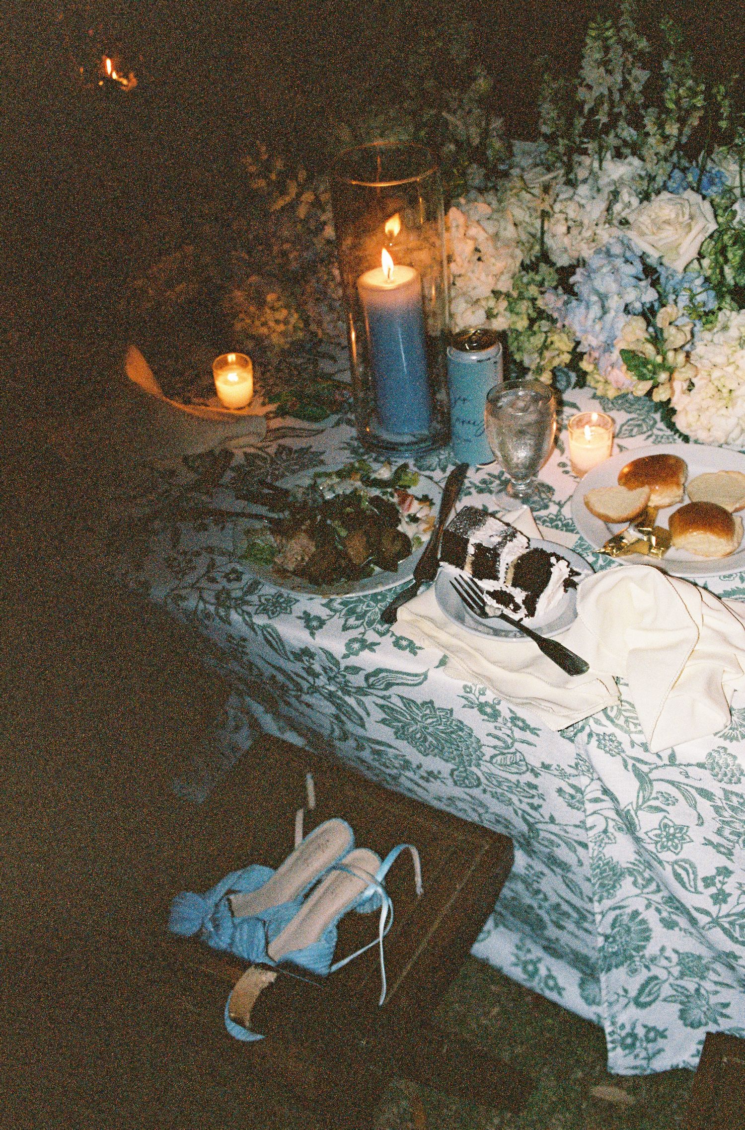 Vintage camera and blue candles arranged on lace tablecloth with flowers creating a romantic nighttime ambiance.