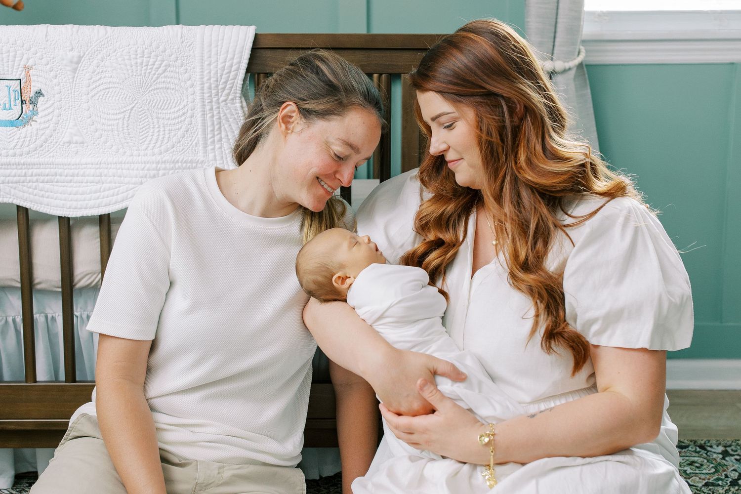 A tender family moment in a nursery as parents lovingly gaze at their newborn baby wrapped in white.