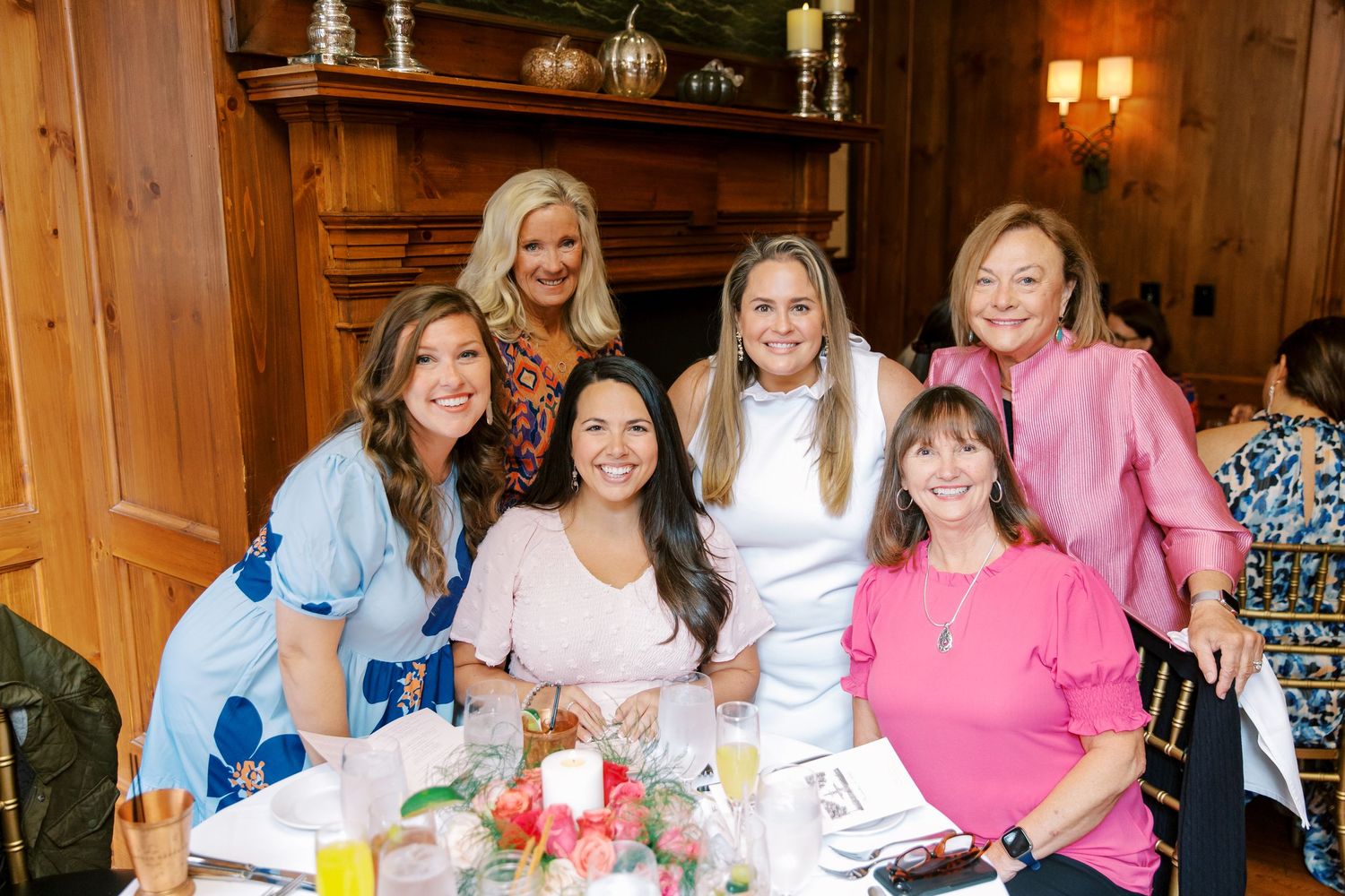 Guests pose together at an elegant table during a celebration in a rustic wood-paneled room.