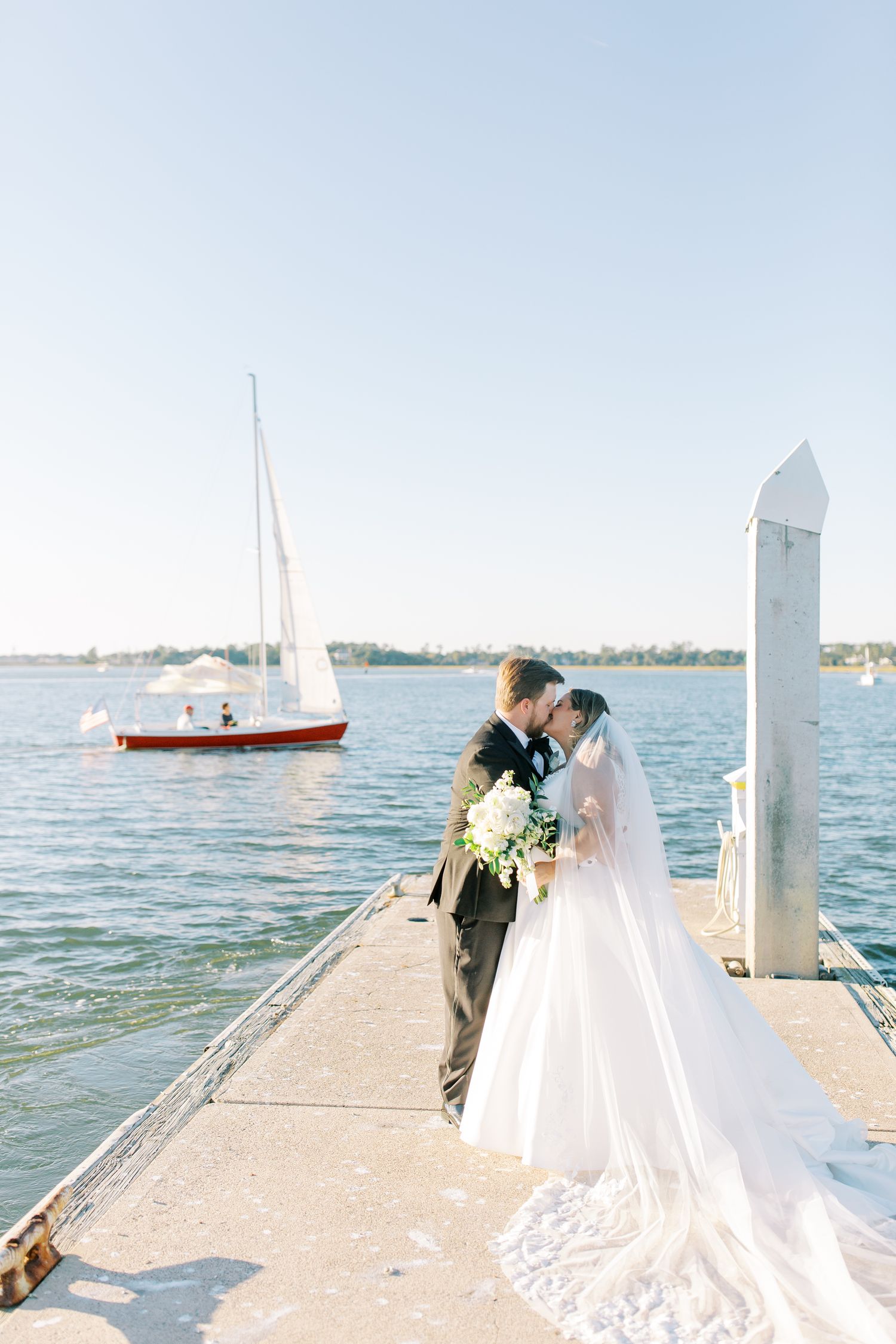 Couple sharing romantic moment on dock with sailboat in background.