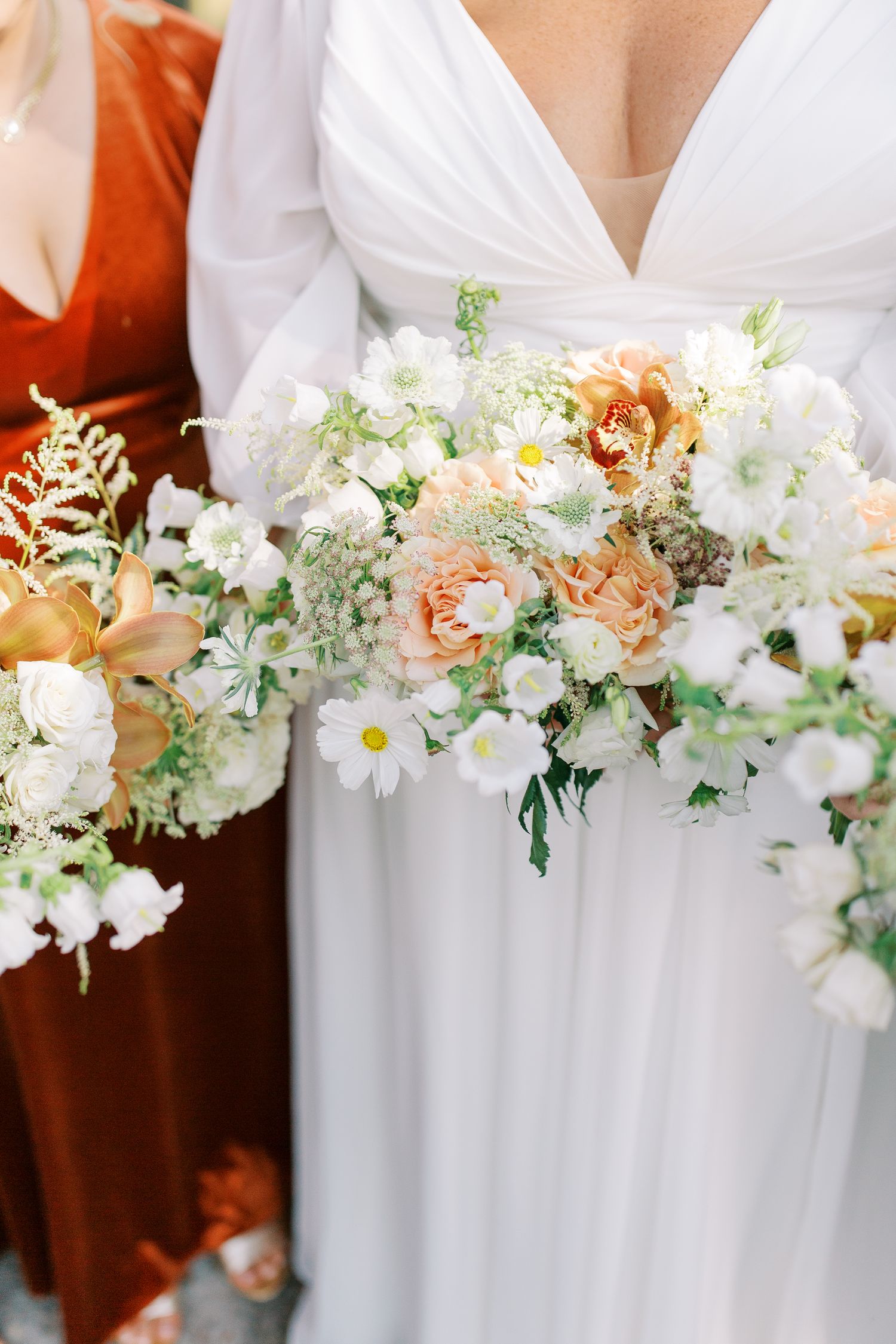 Beautiful peach and white bridal bouquet with roses and mixed flowers against white dress.