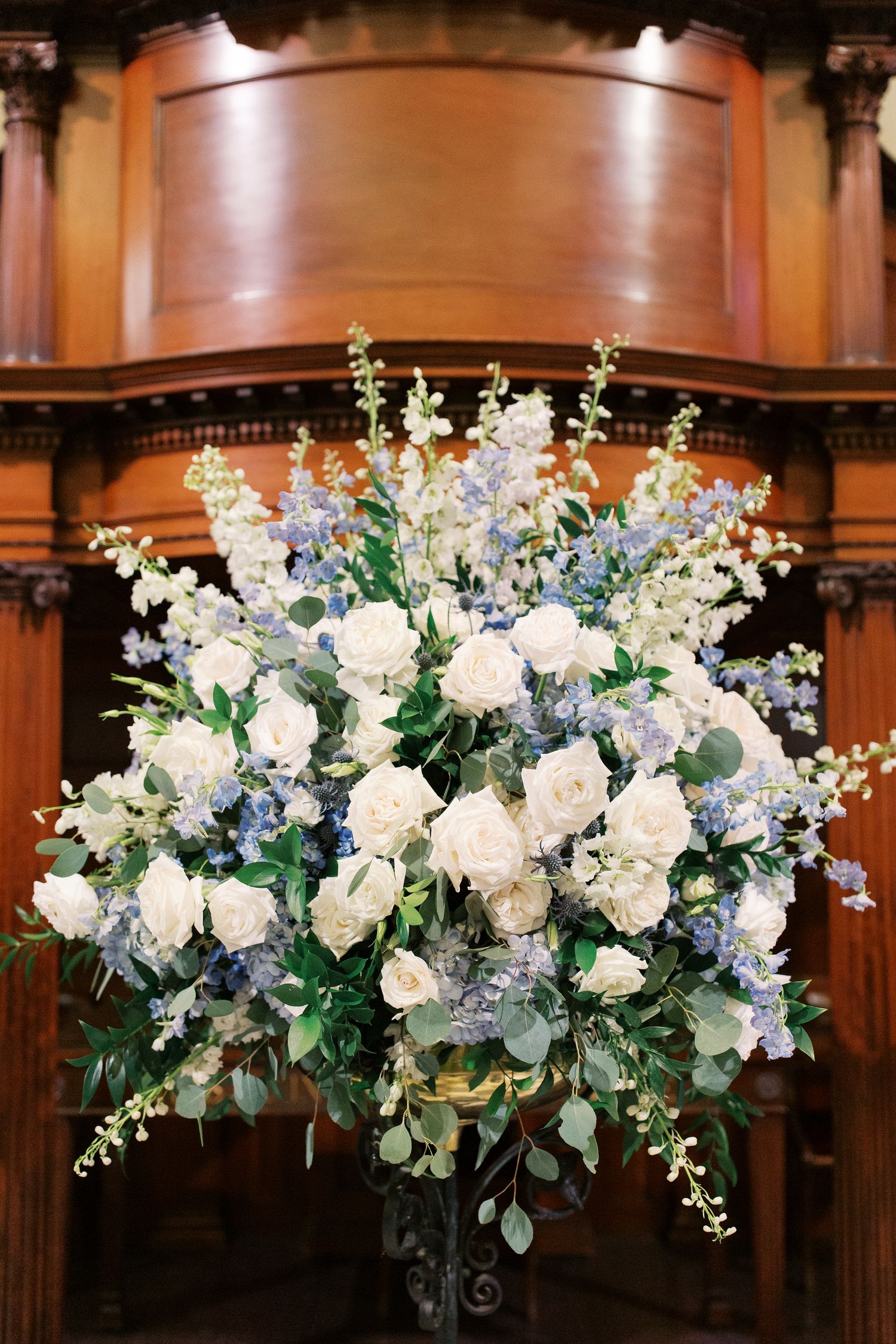 Luxurious white and blue floral arrangement with roses and delphinium on wooden altar.
