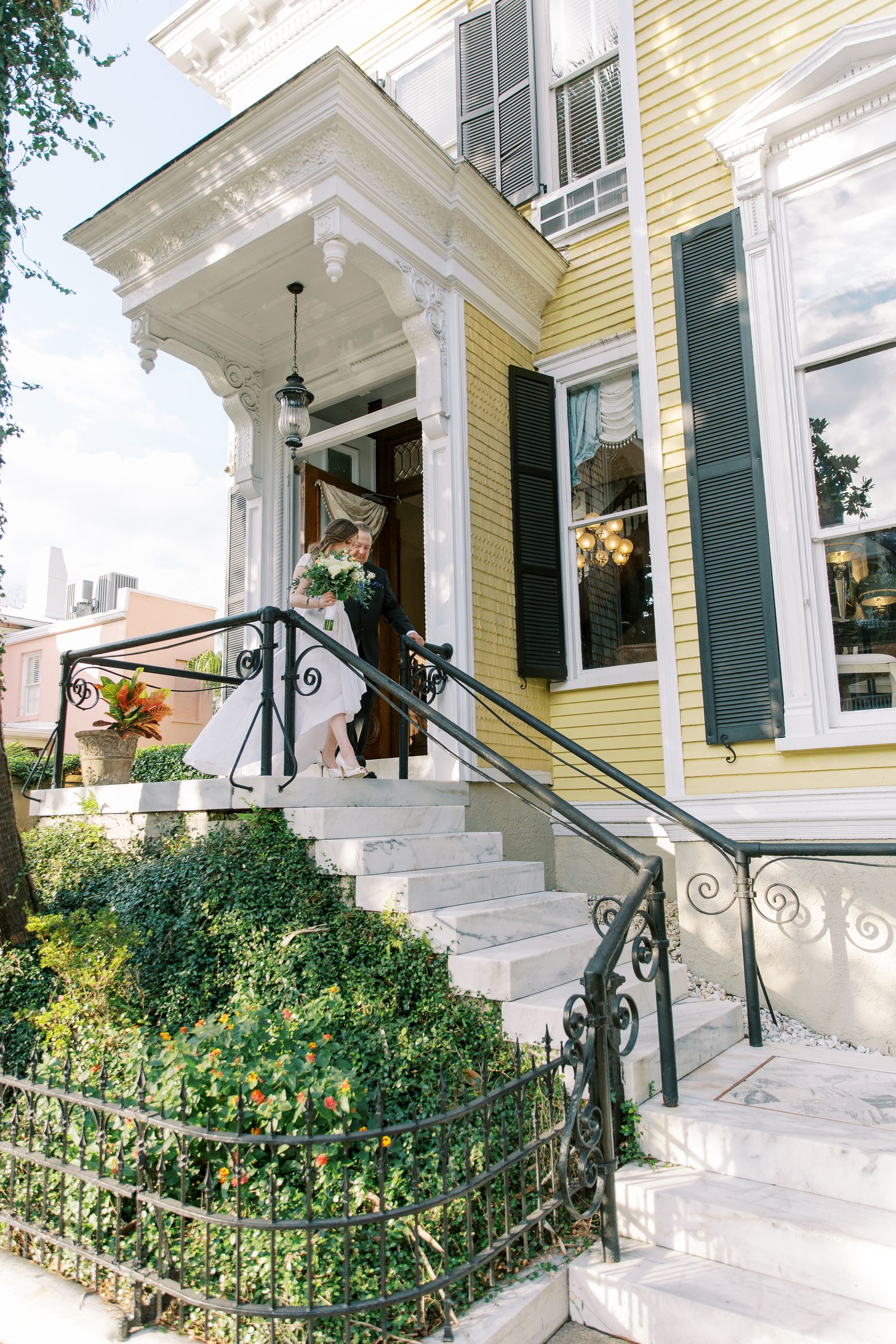 Exterior view of a classic yellow house with white trim and ornate iron railings on the front steps.