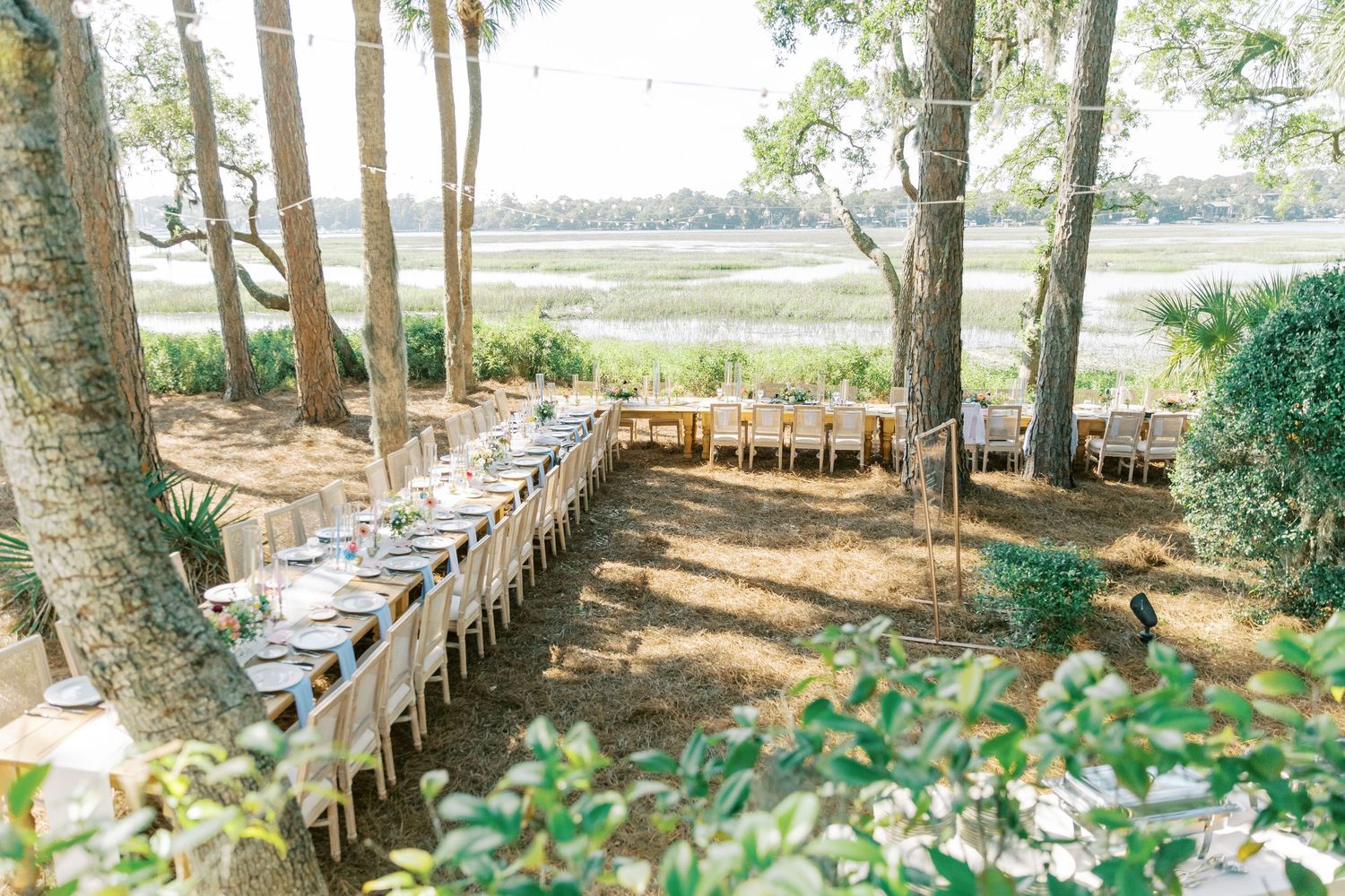 Long rustic dining tables set up under trees for outdoor wedding reception.