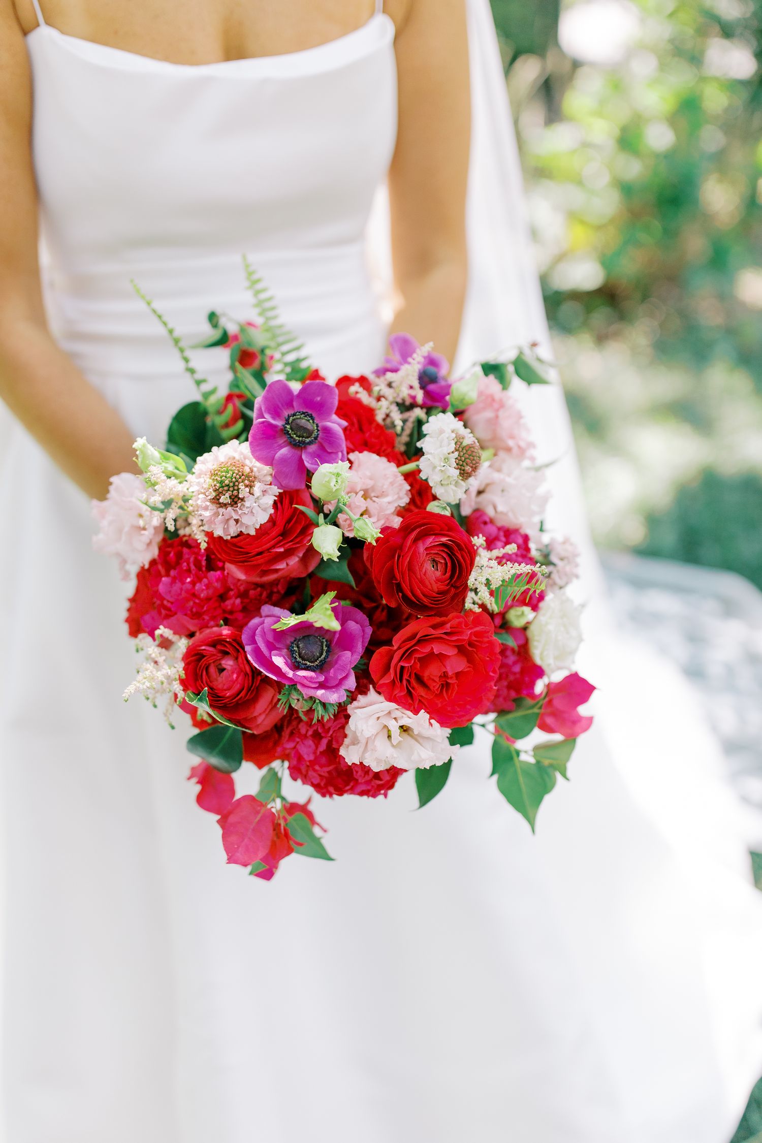 A vibrant wedding bouquet with red and pink flowers against a white wedding dress.