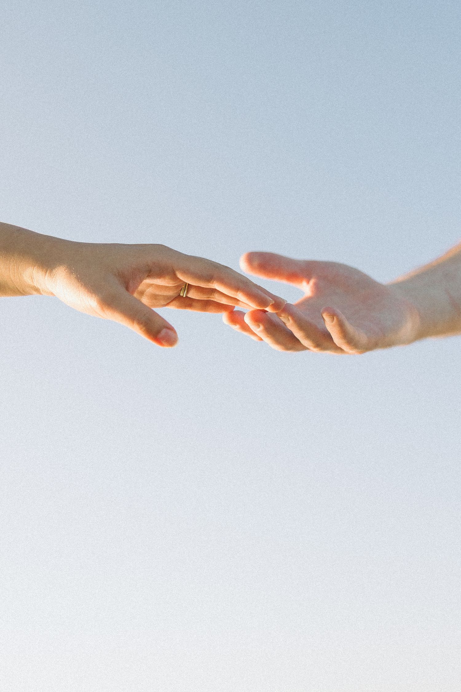 Two hands reaching towards each other against a bright sky background in a symbolic gesture of connection and unity.