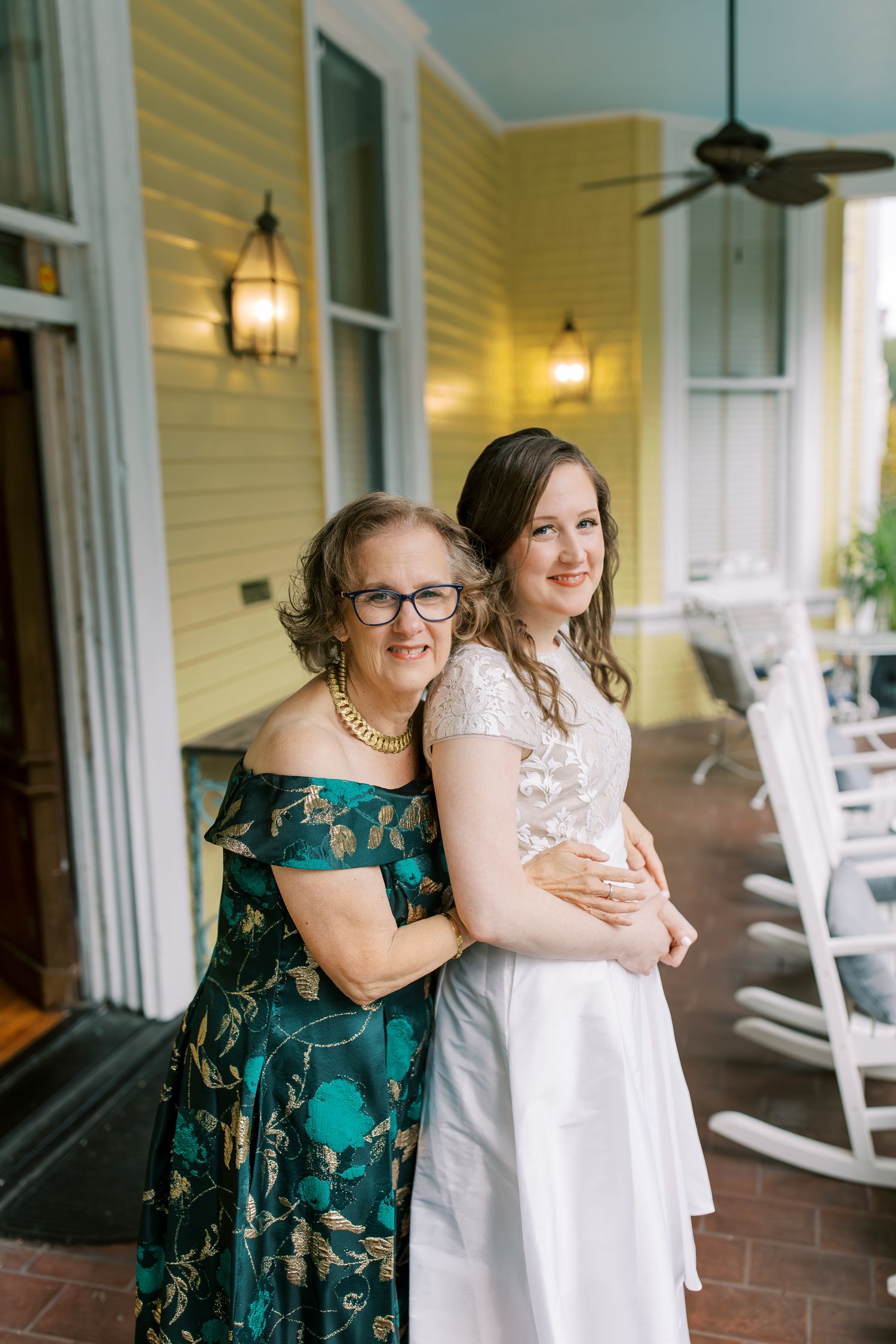 A touching moment on a charming southern porch with white rocking chairs and yellow siding.