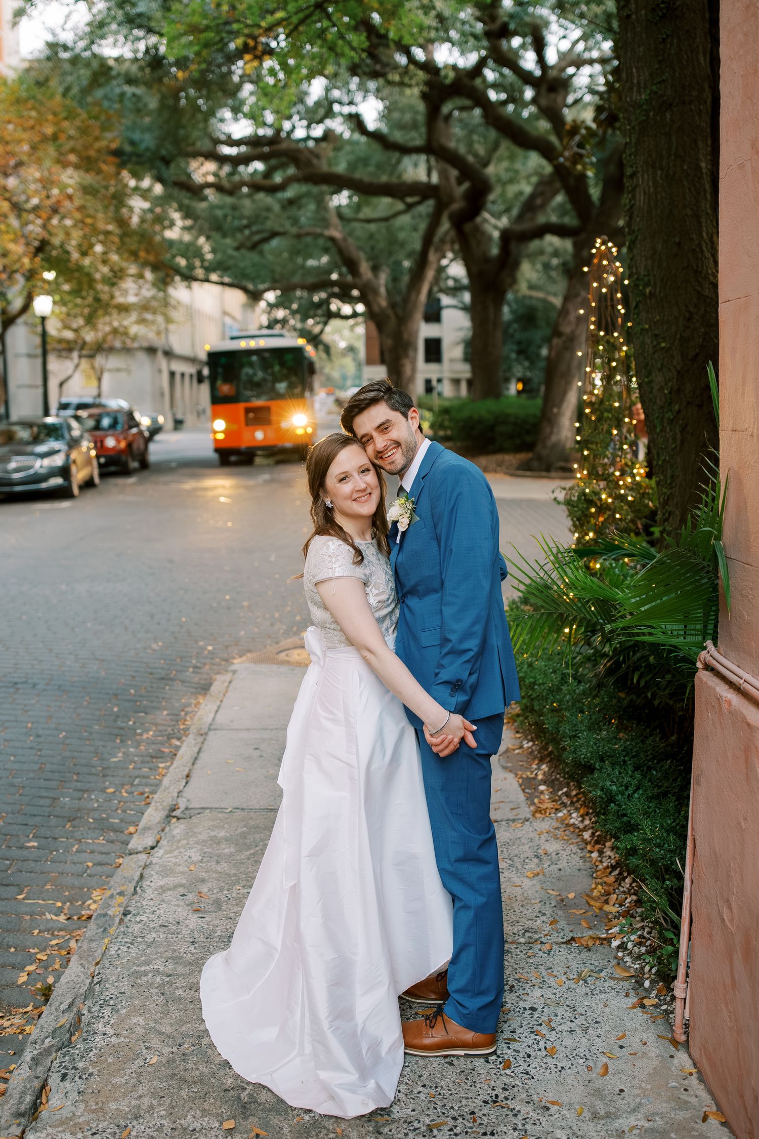 Romantic evening wedding portrait with twinkling lights and trees in the background.