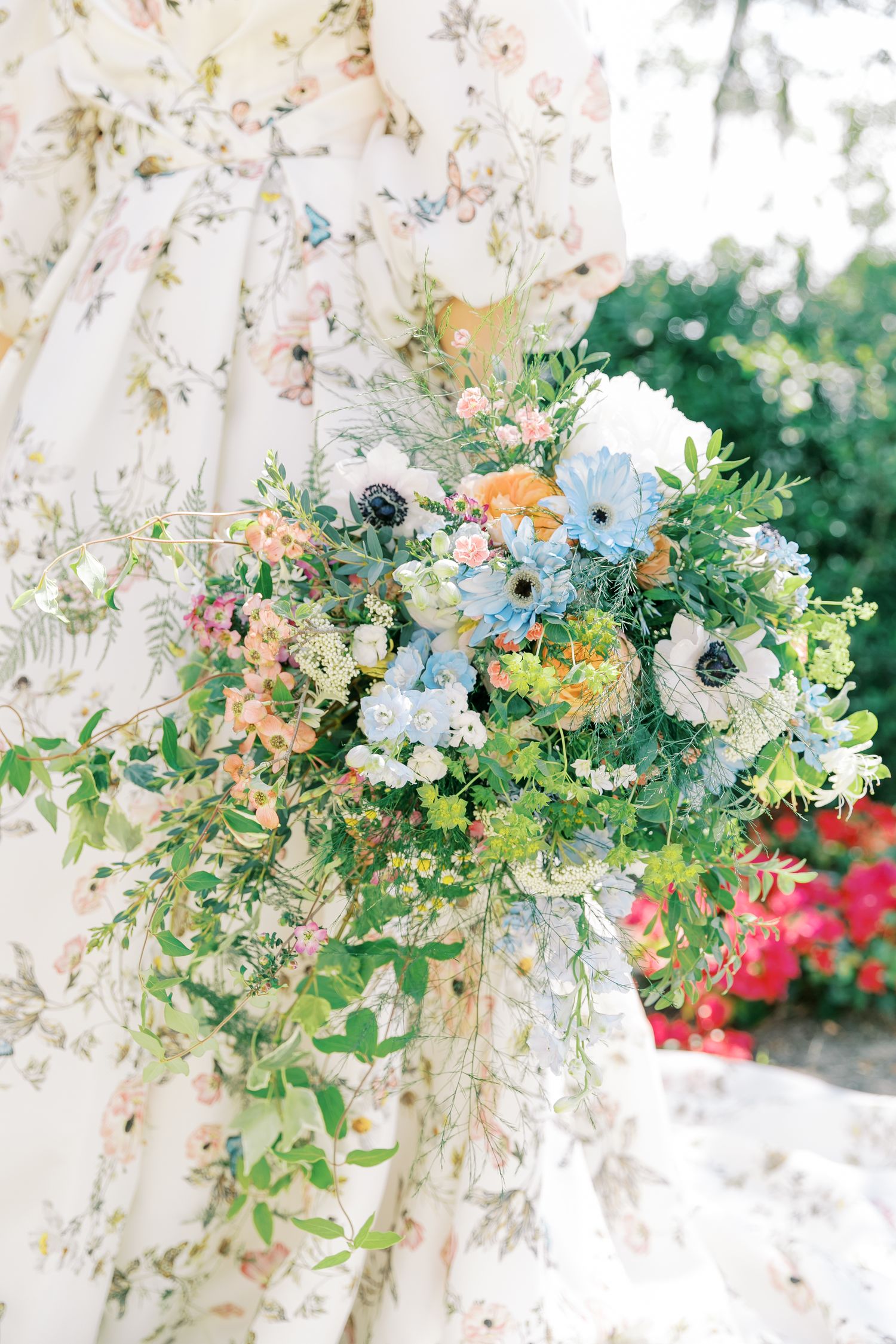 Elegant floral arrangements with white and peach blooms mixed with greenery hang from white structures at an outdoor venue.