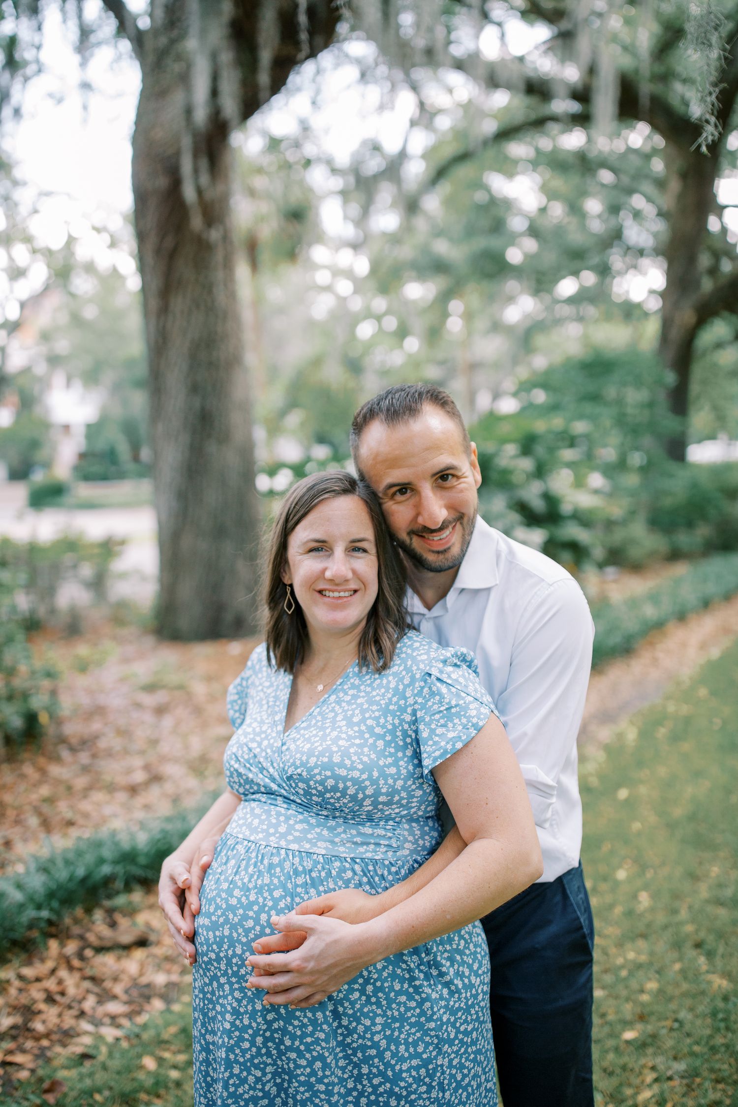 A joyful maternity shoot featuring a couple embracing under Spanish moss trees.