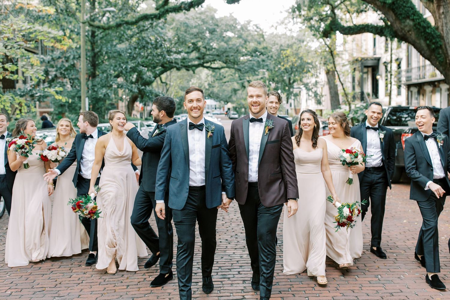 Wedding party walks together down tree-lined path with bridesmaids in blush dresses and groomsmen in dark suits.