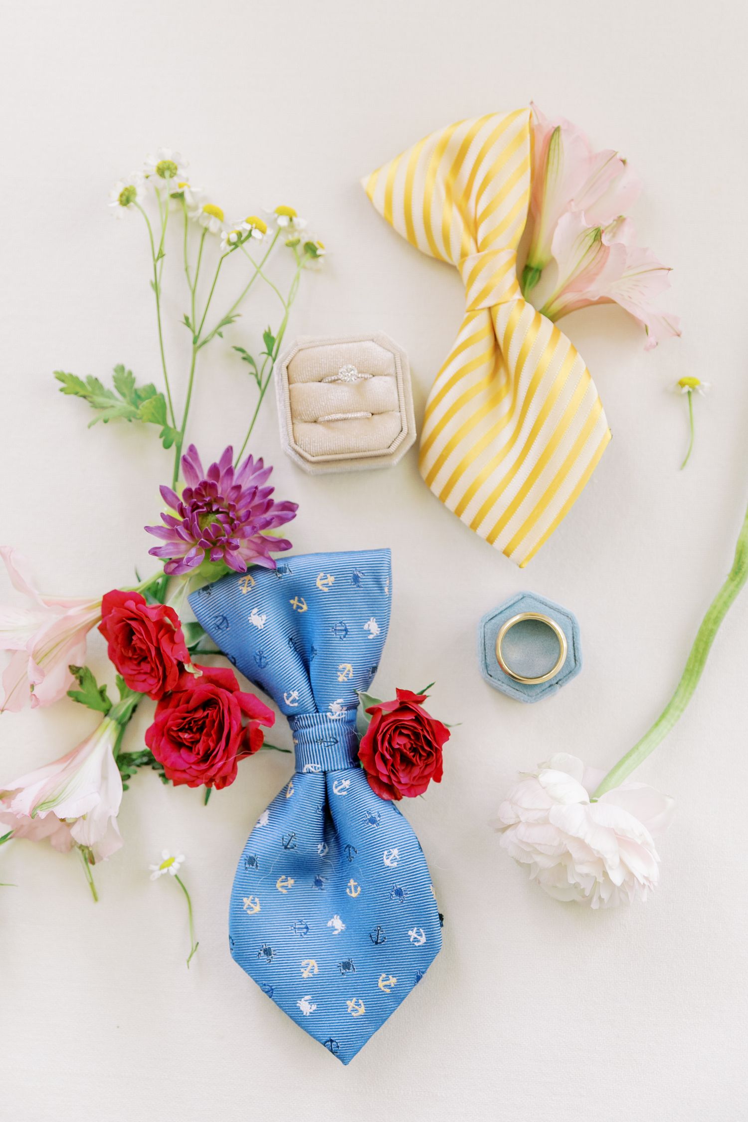 Wedding accessories including yellow and blue bowties, rings, and fresh flowers arranged on light background.