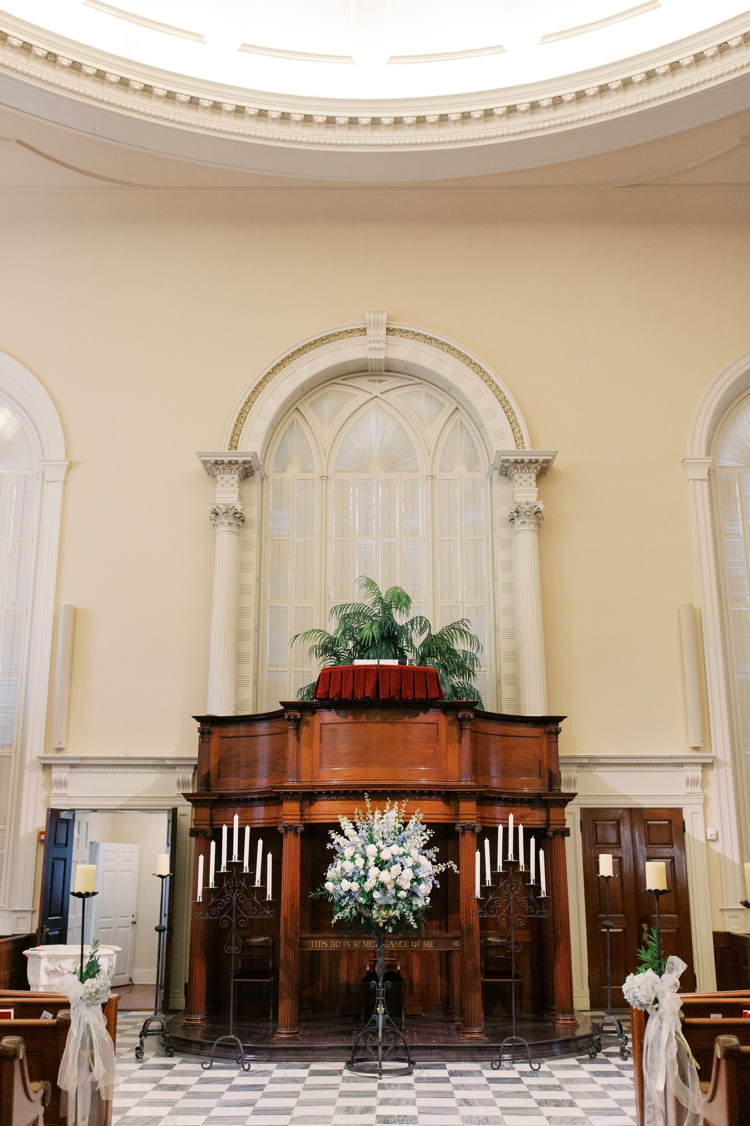 Elegant church interior with wooden pews and white floral arrangements under a domed ceiling.