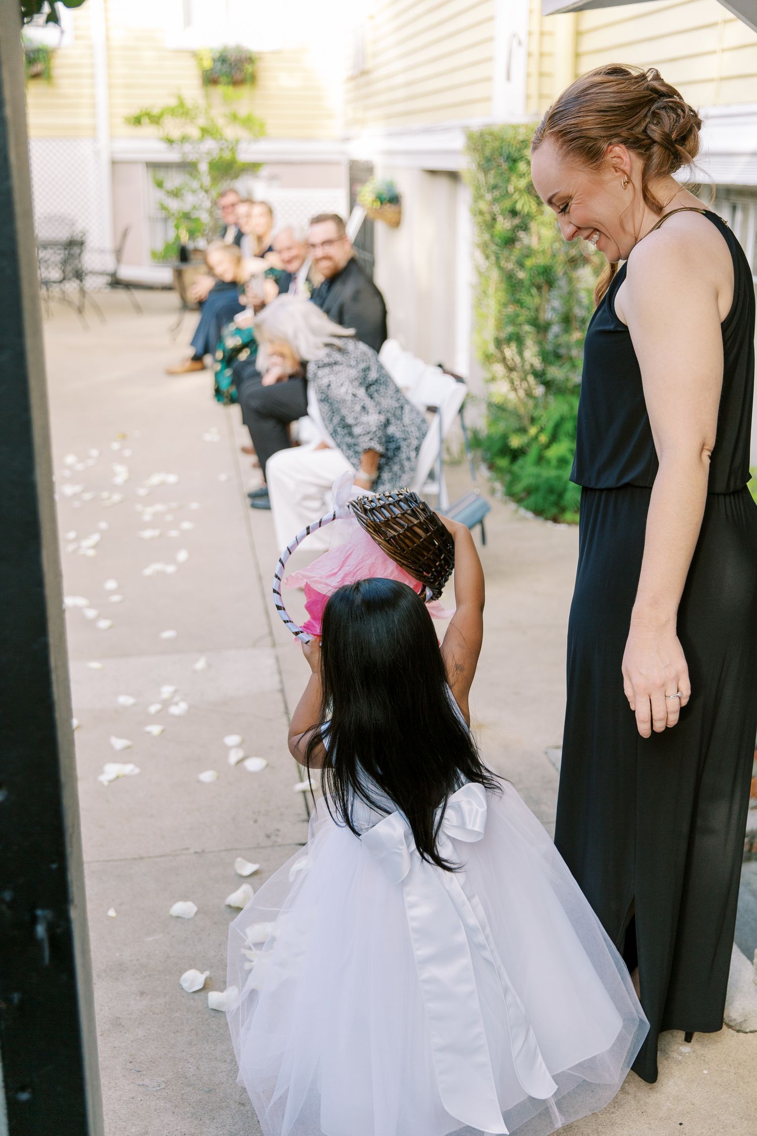 Young girls in black and white dresses playing with scattered flower petals on a garden path.