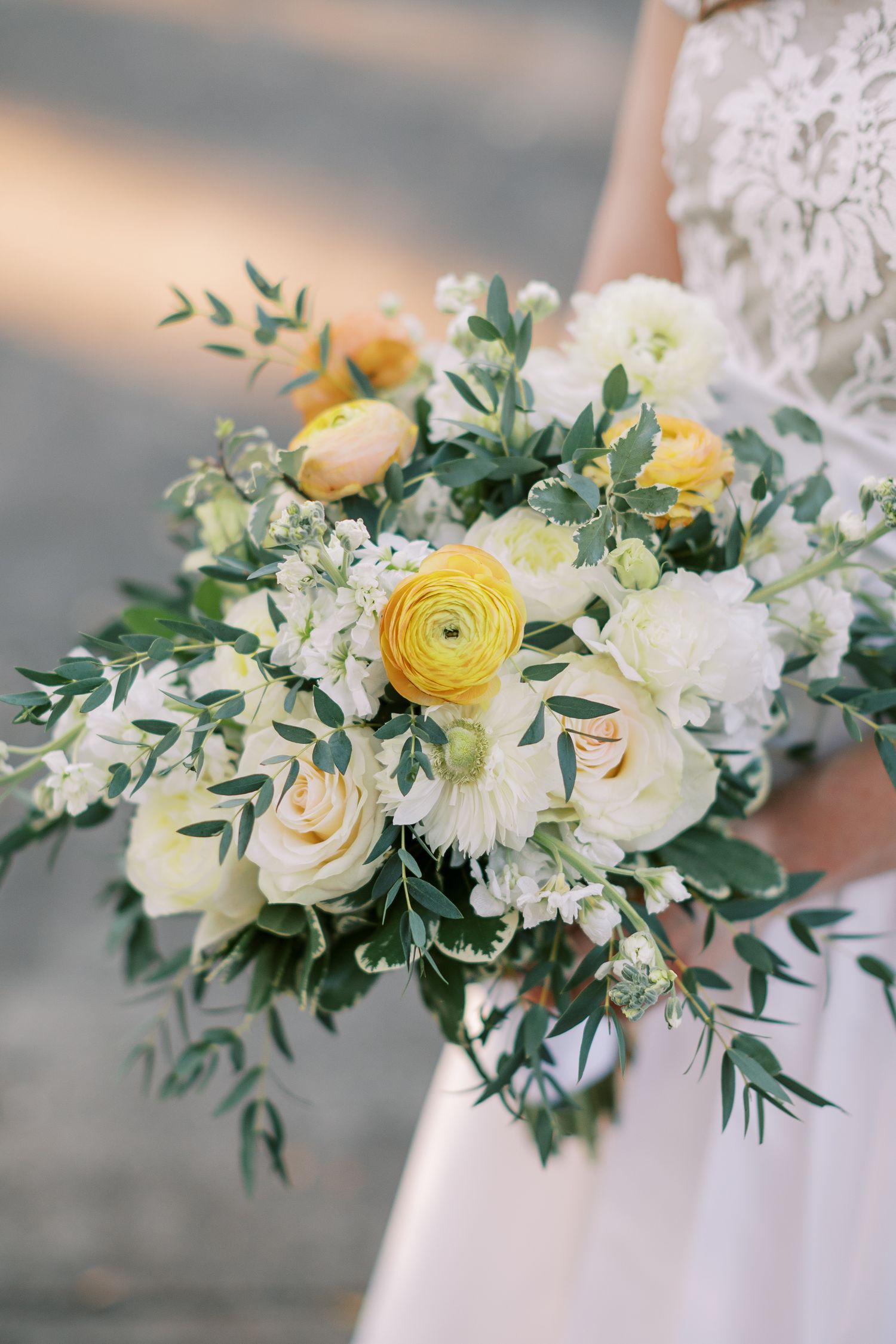 Elegant bridal bouquet featuring yellow ranunculus, white roses, and delicate greenery.