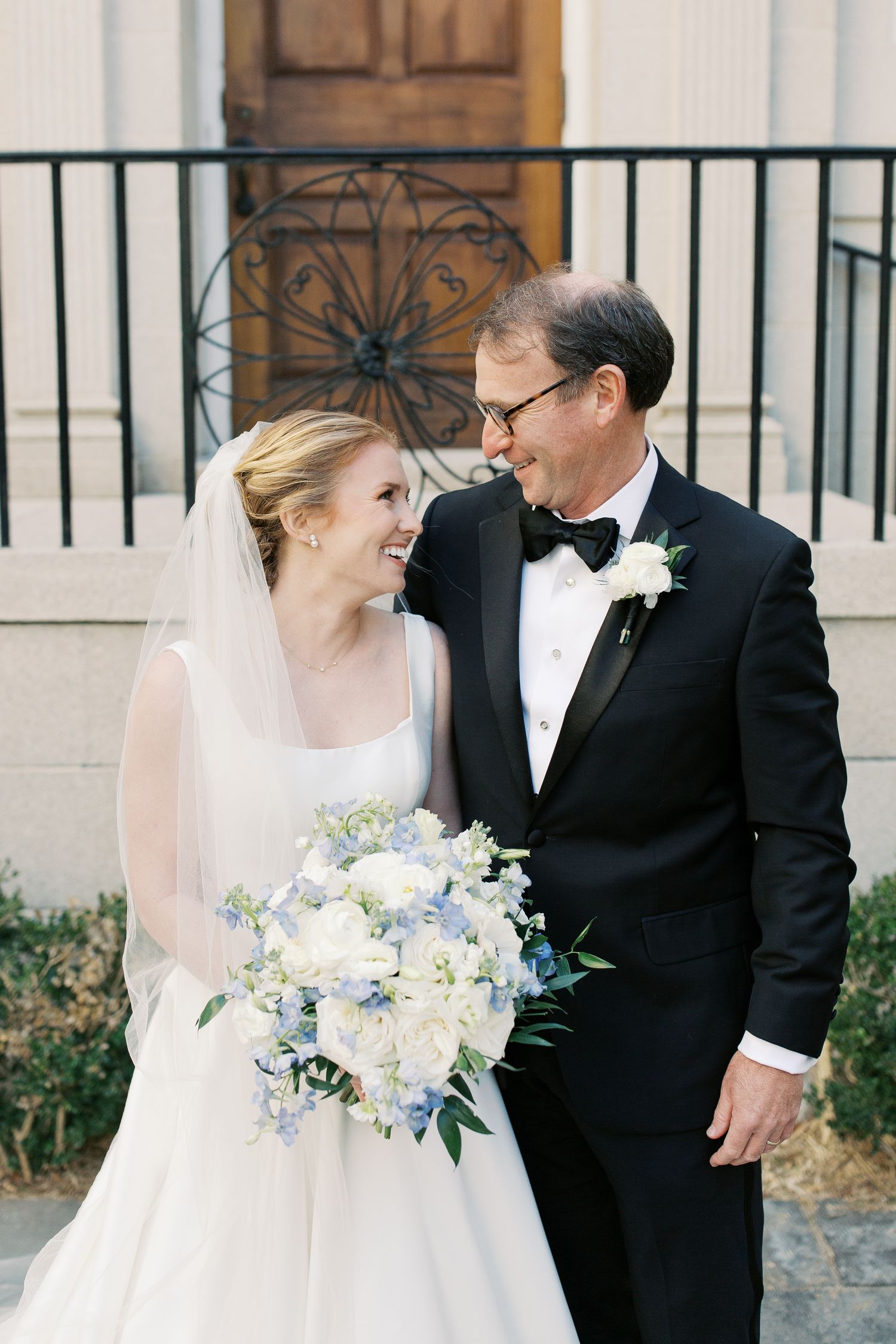 Elegant wedding couple poses against white building with black iron railings.
