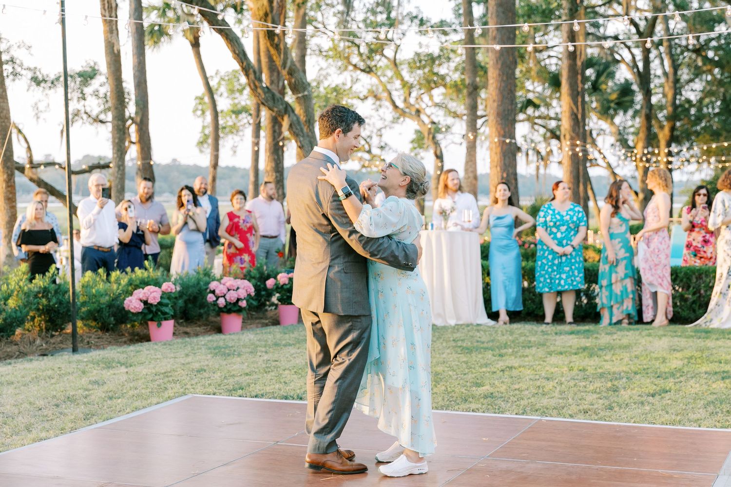 Wedding guests standing alongside a tree-lined path during an outdoor ceremony.