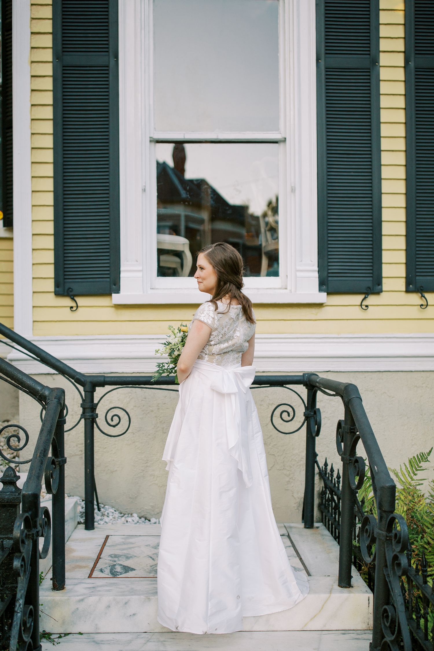 White wedding dress flowing over iron railings on a historic yellow building's porch.