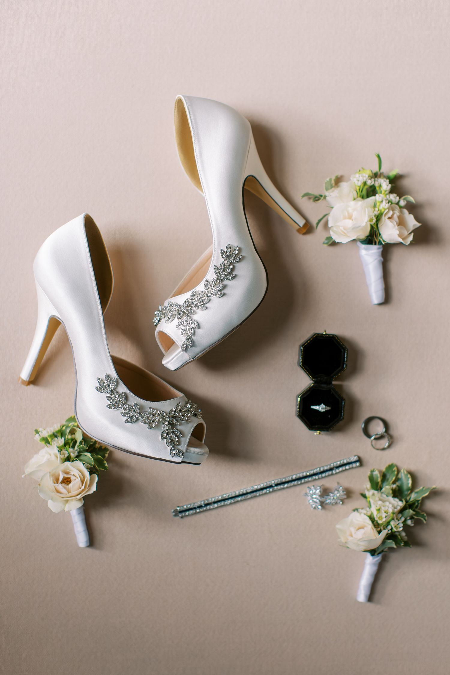 Elegant white bridal shoes with silver embellishments displayed alongside delicate roses and accessories.