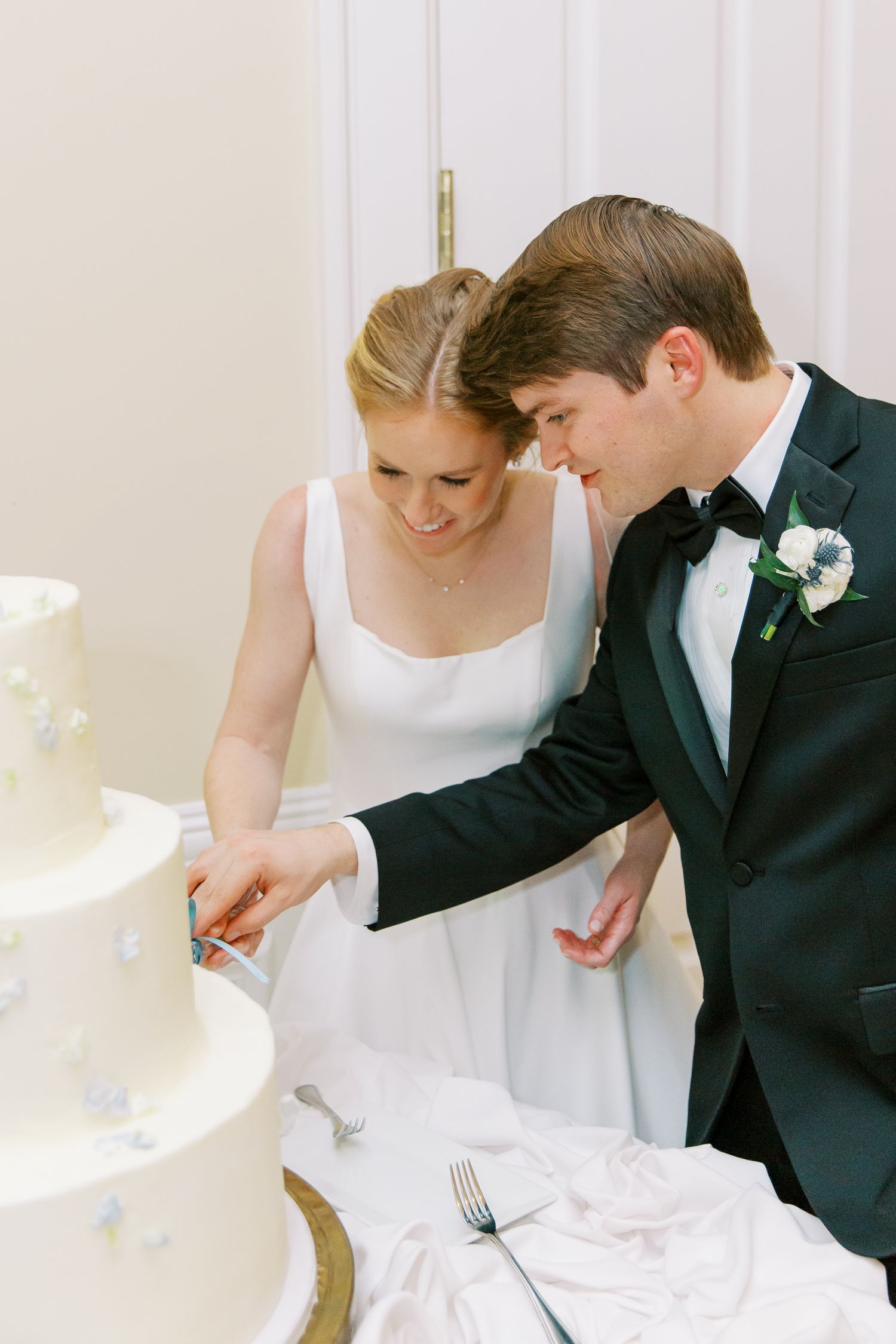Wedding couple cutting their elegant white tiered cake together at the reception.