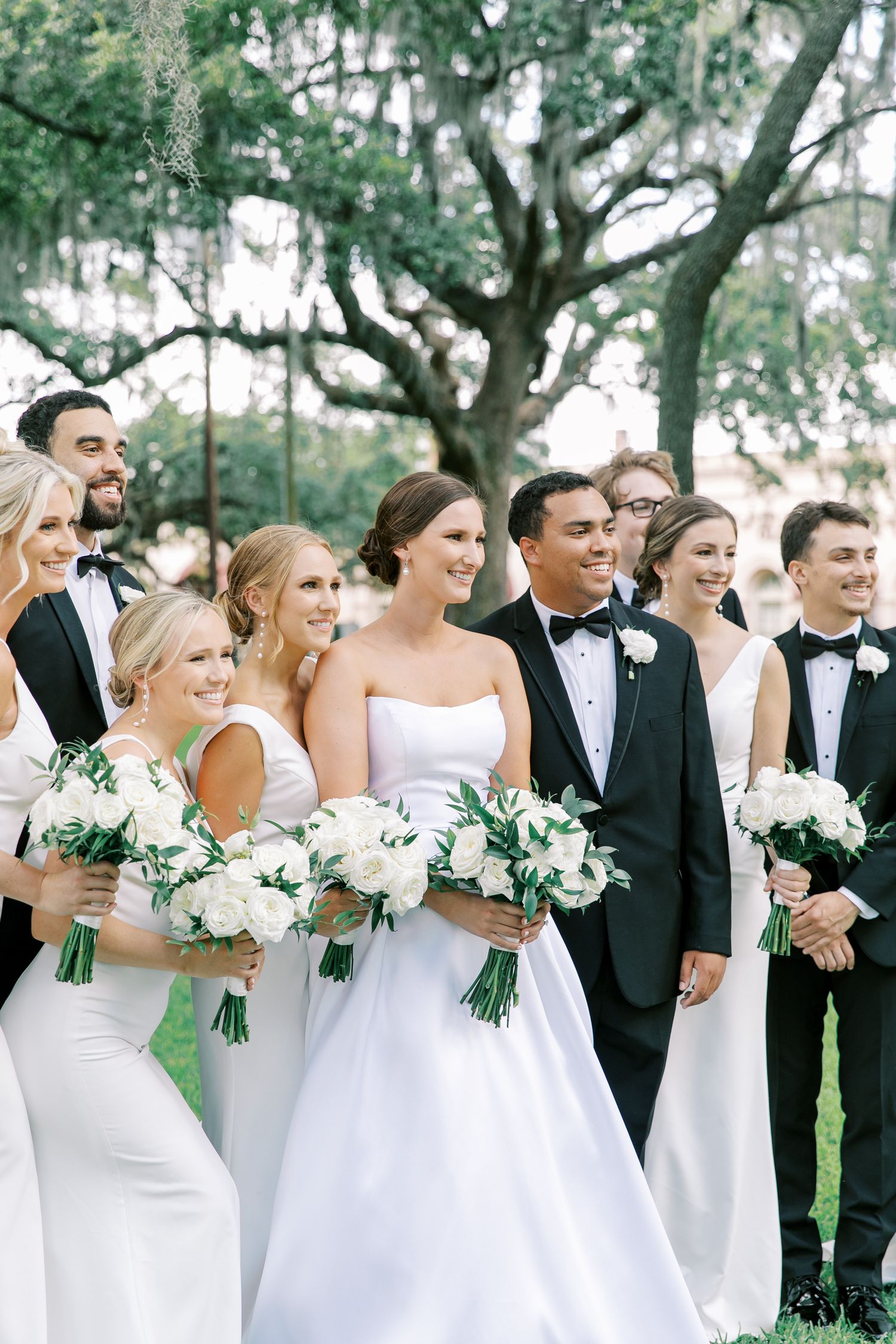 Wedding party poses outdoors under Spanish moss trees with white floral bouquets in Emmett Park.