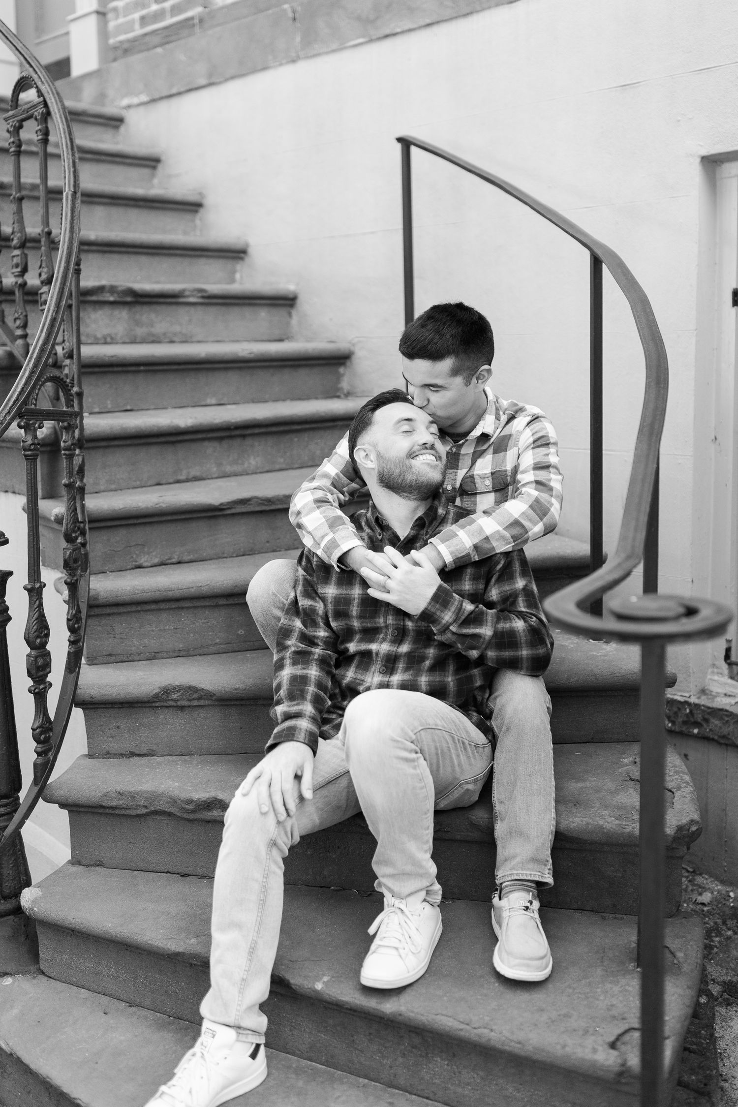 Intimate gay couple portrait on stone steps featuring matching plaid shirts and casual style.