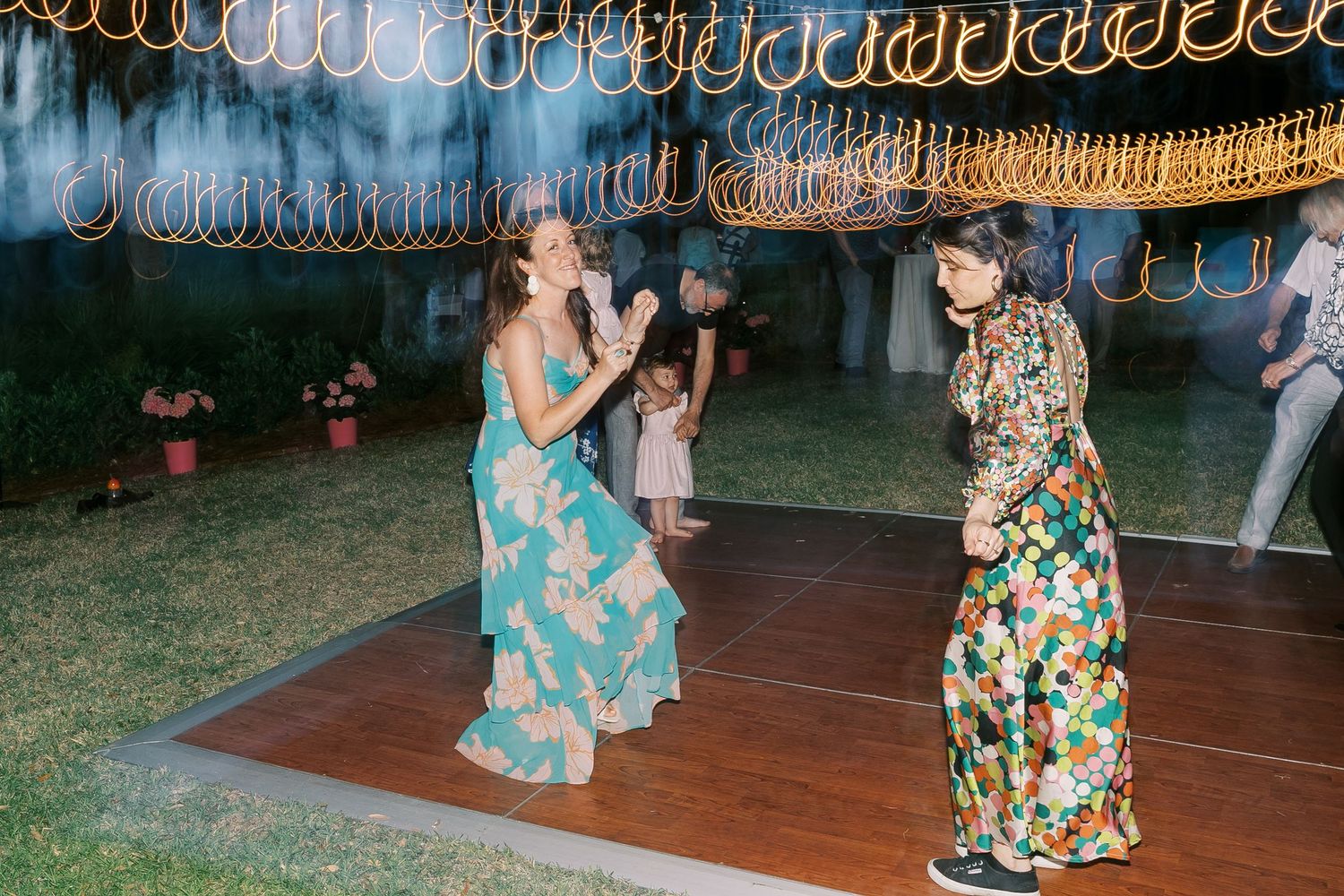 Evening dance party with string lights and people dancing in floral dresses.