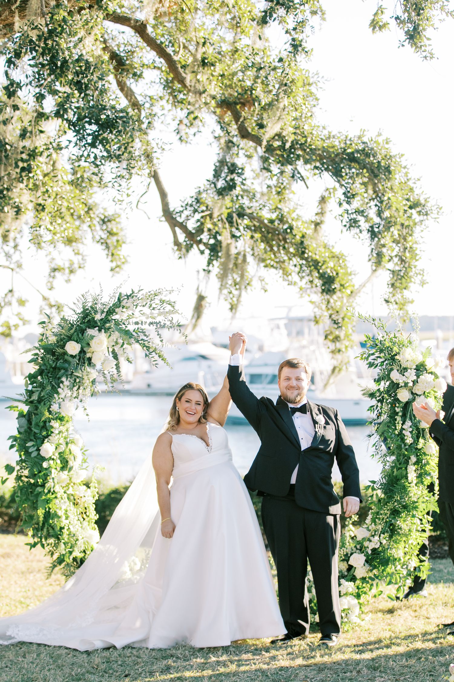 A celebratory moment under a floral arch with waterfront views in the background.