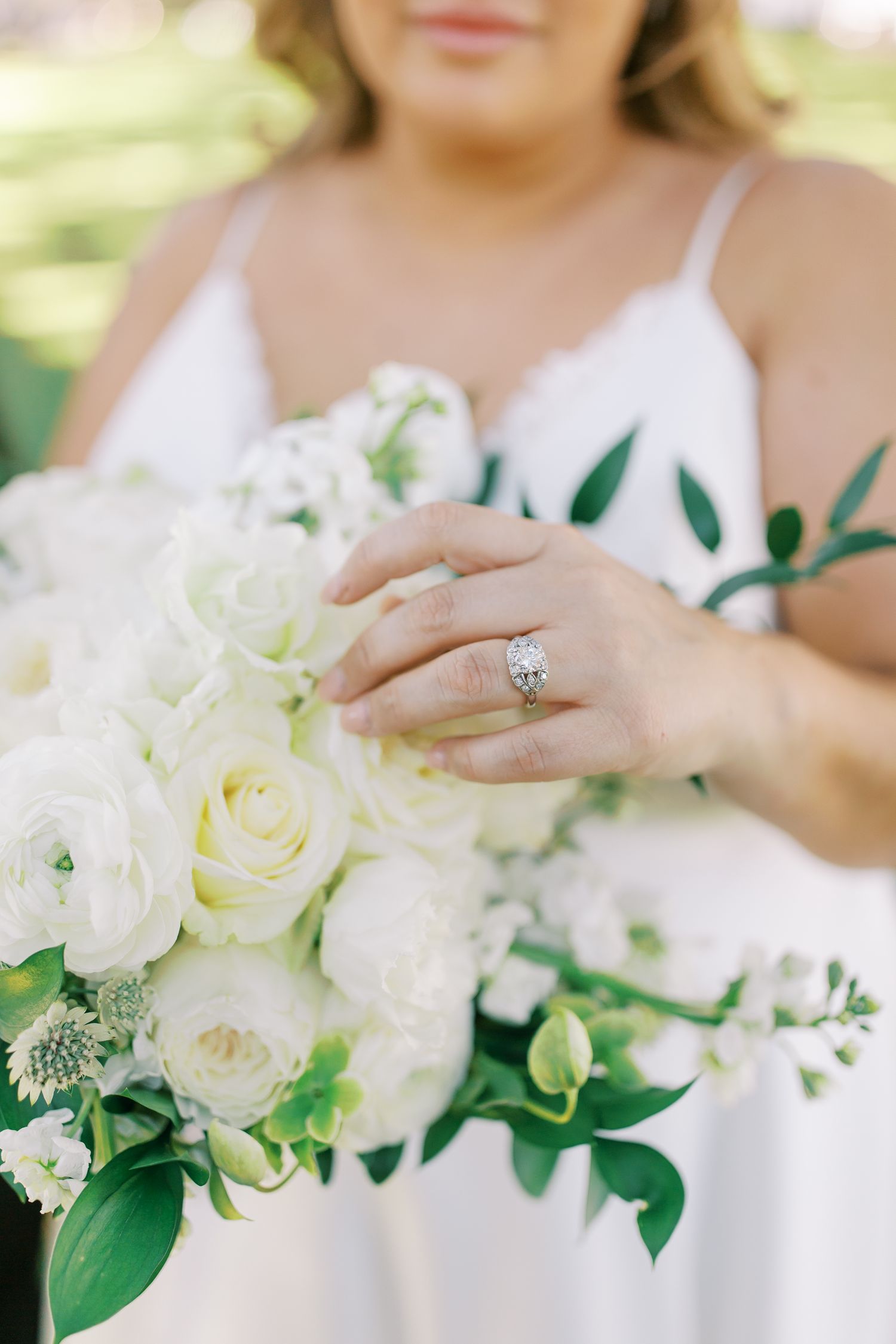 Close-up of a white rose bouquet and engagement ring against a white wedding dress.