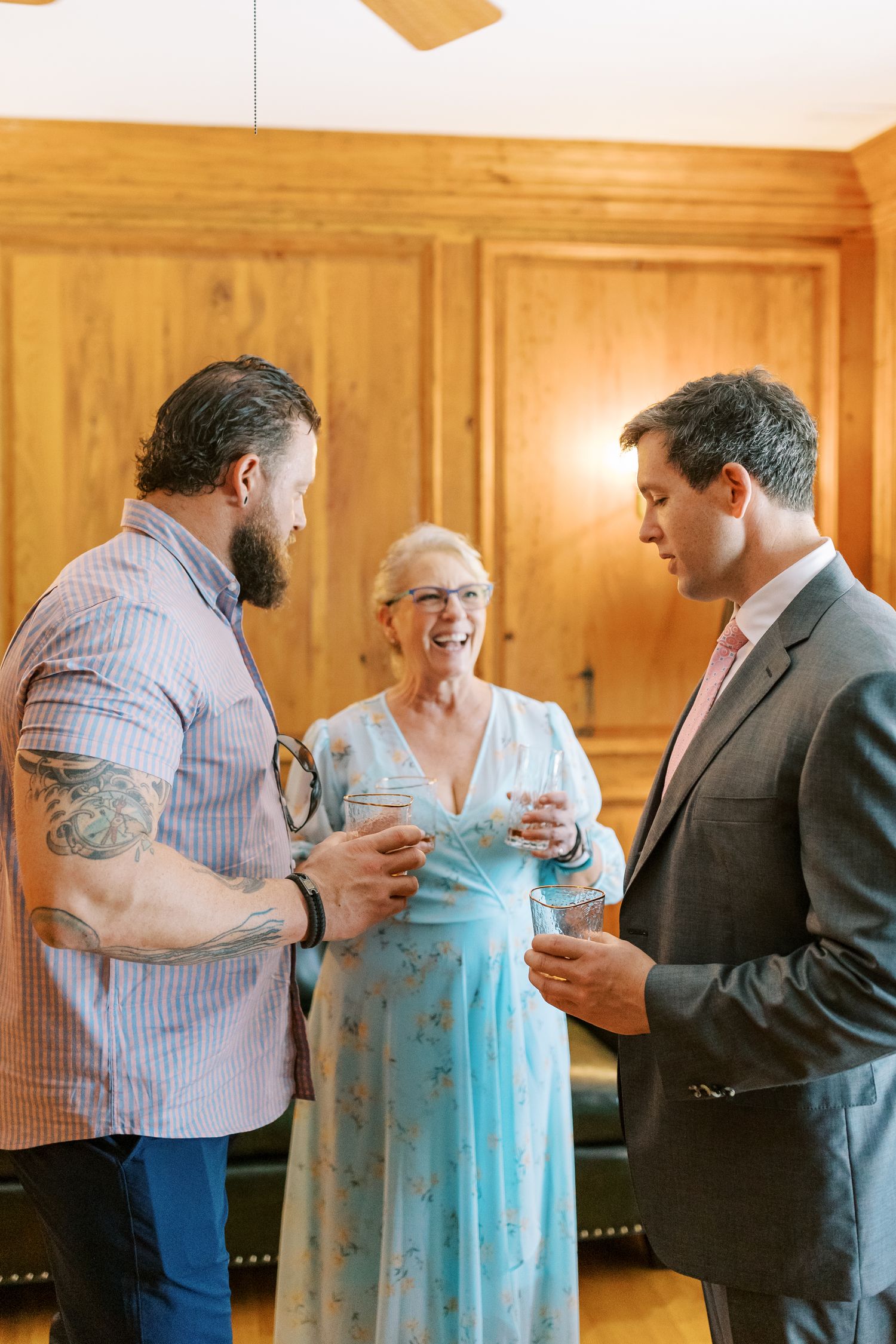 Three people having drinks and conversing in a wood-paneled room at a formal event.